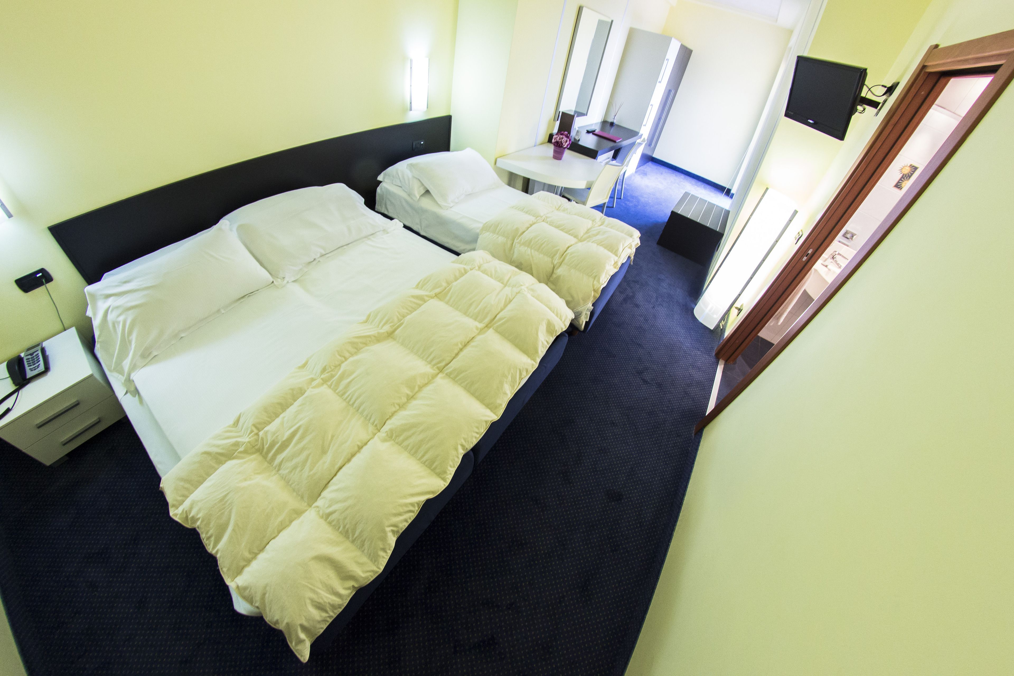 Una camera d'albergo con due letti, una scrivania, una sedia, una televisione e una porta.