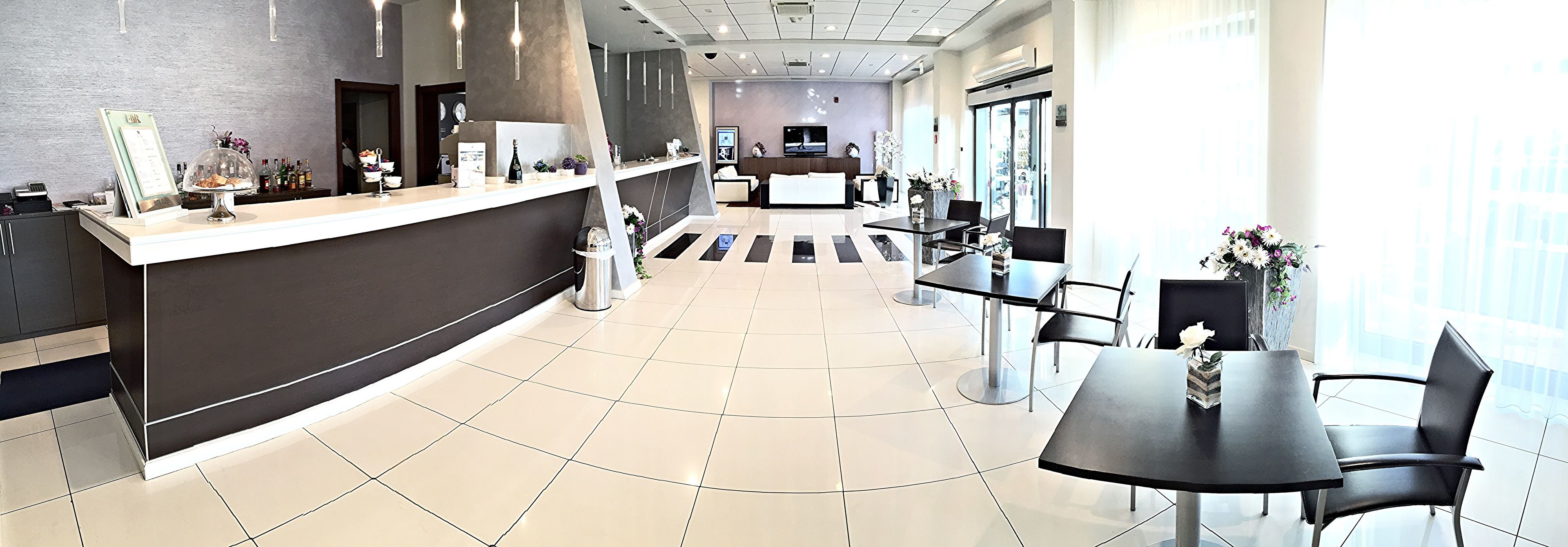 A modern hotel lobby with a reception desk, seating area, and large windows.