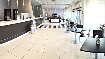 A modern hotel lobby with a reception desk, seating area, and large windows.