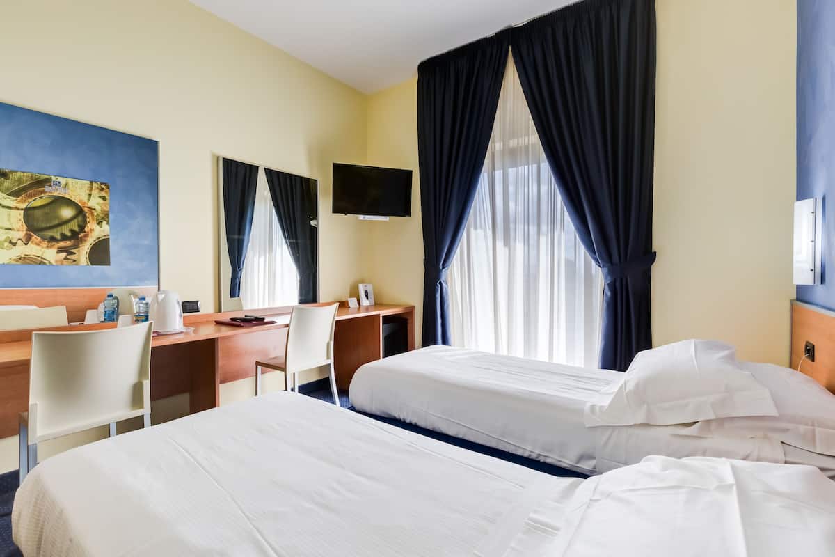 A hotel room with two beds, a desk, a chair, a television, and a large window with curtains.