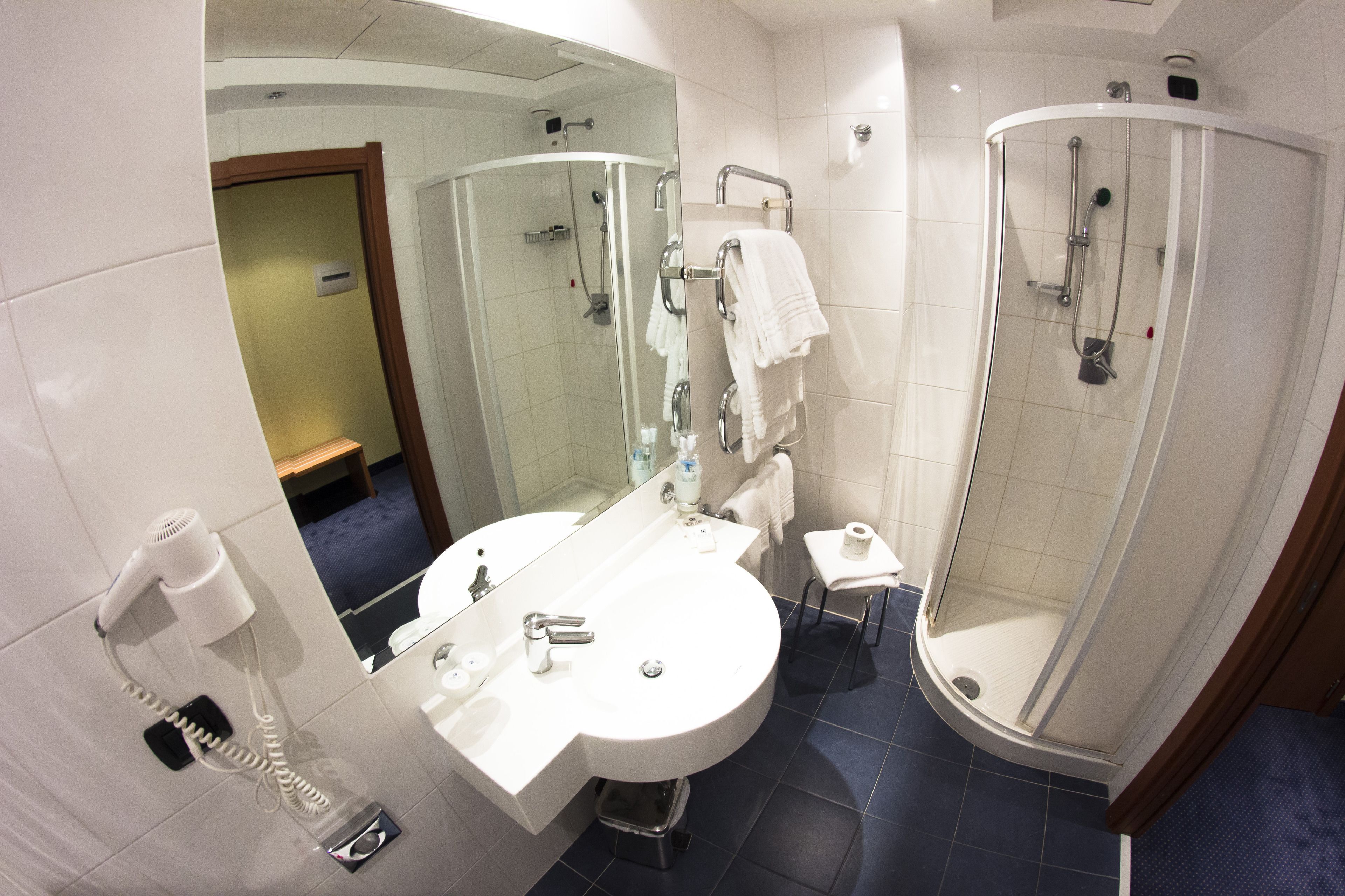 Une salle de bain moderne dotée d’un grand lavabo, d’un miroir, d’un sèche-cheveux et de deux douches en verre.