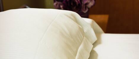 A bed with white linens and a bouquet of purple flowers in the background.
