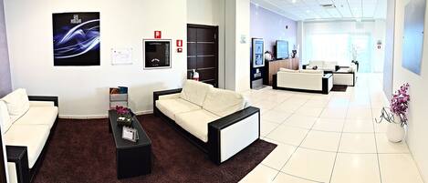 Una hall d'albergo moderna con reception, area salotto e un'ampia vetrata che lascia entrare la luce naturale.