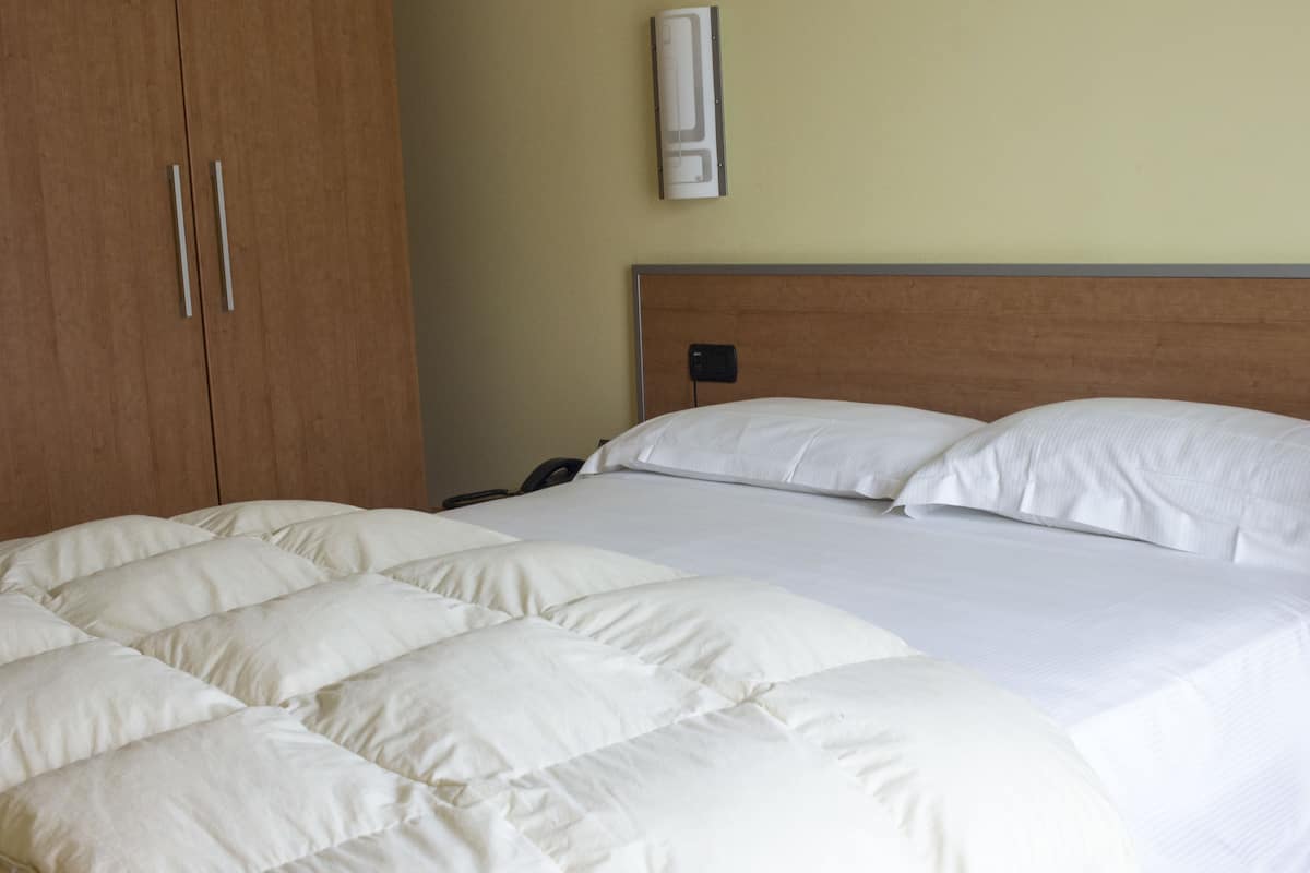 A hotel room with a large bed, wooden wardrobe, and a wall-mounted air conditioning unit.