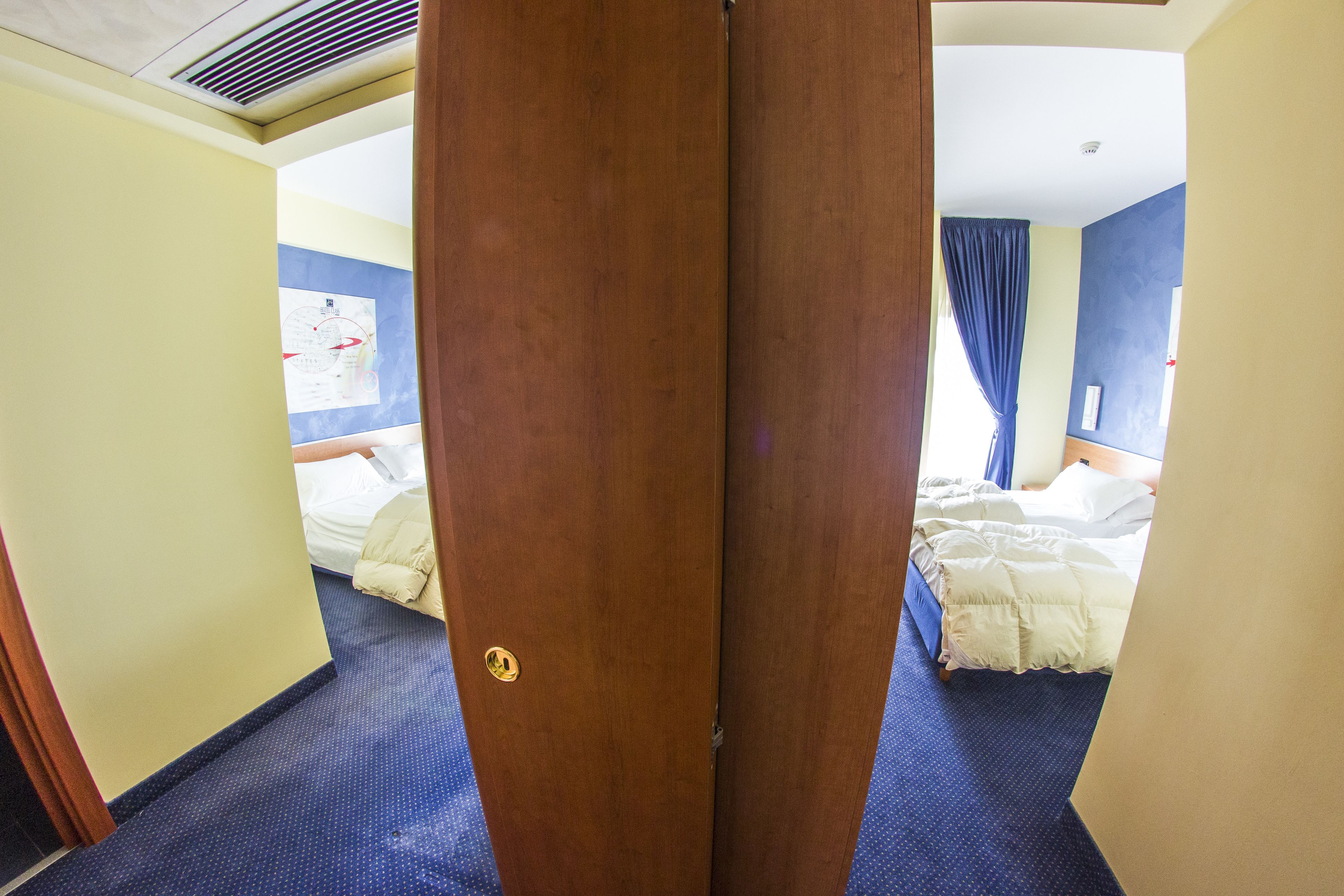 A hotel room with two beds, a wooden door, and a blue carpet.