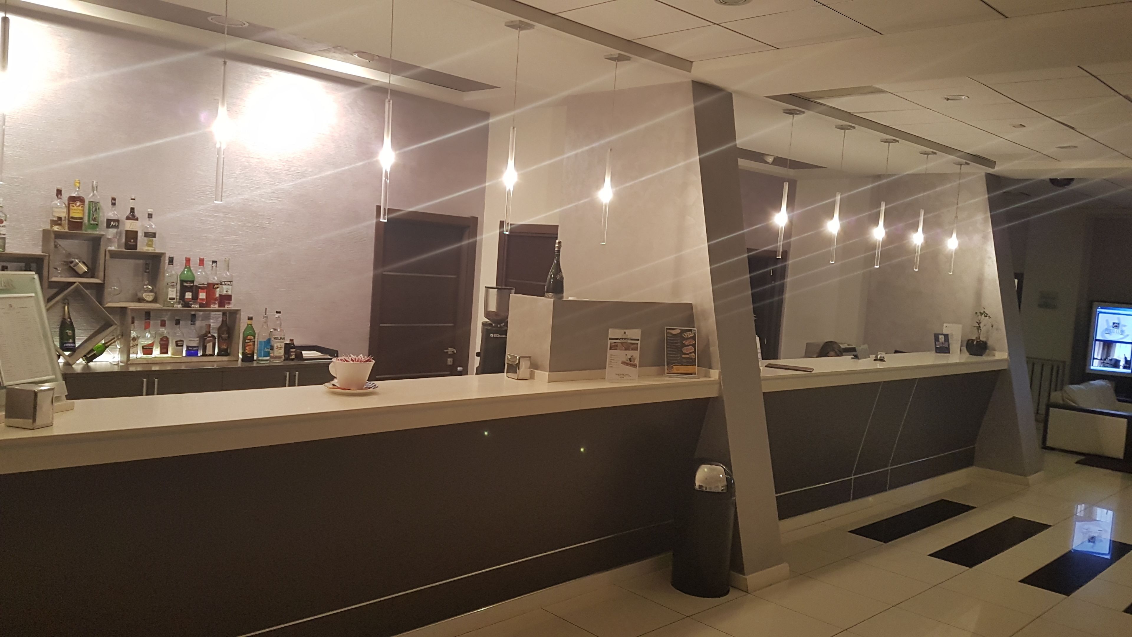 Una zona de recepción moderna con mostrador, varias botellas, una máquina de café y un cubo de basura.