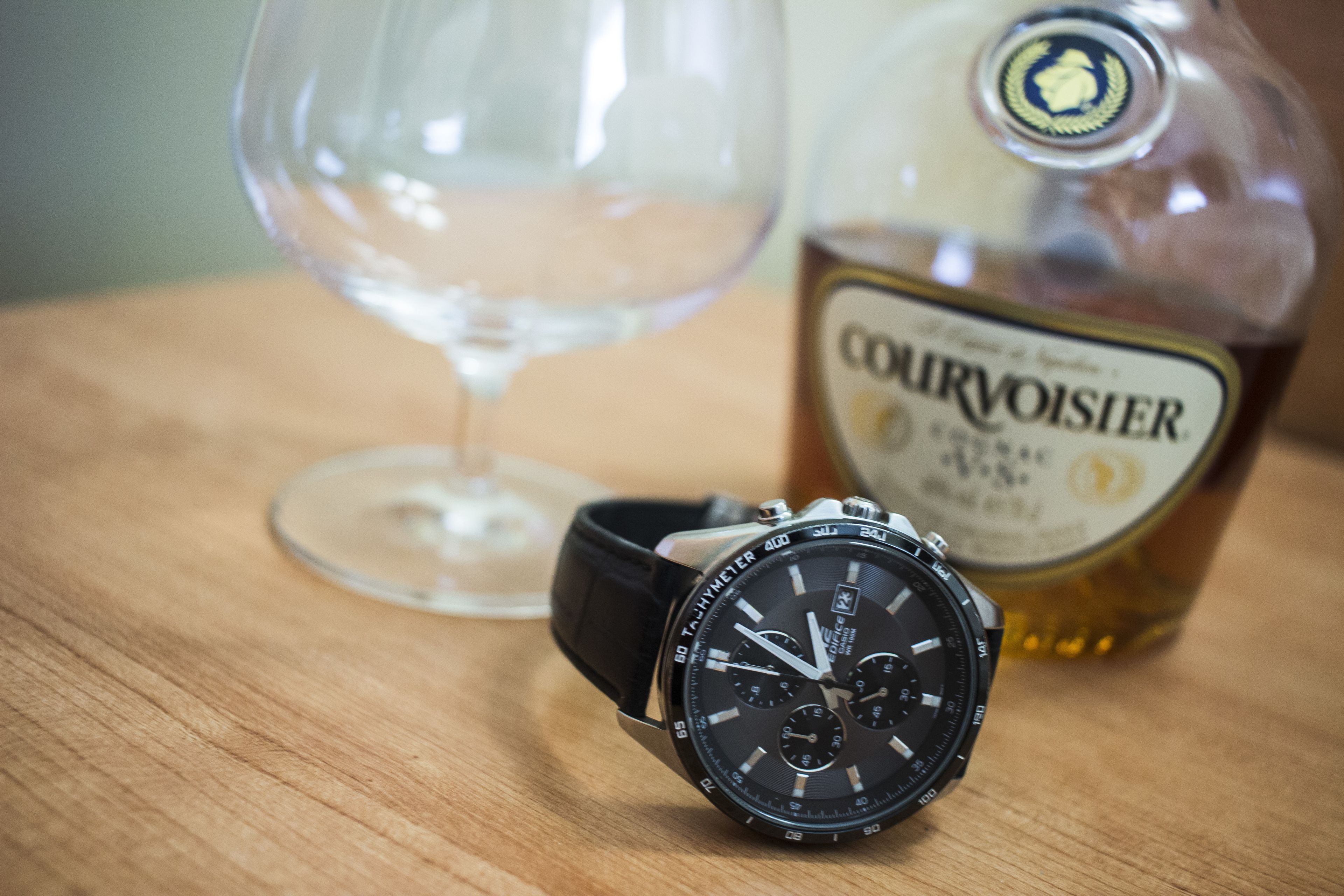 A watch and a bottle of Courvoisier on a wooden surface.