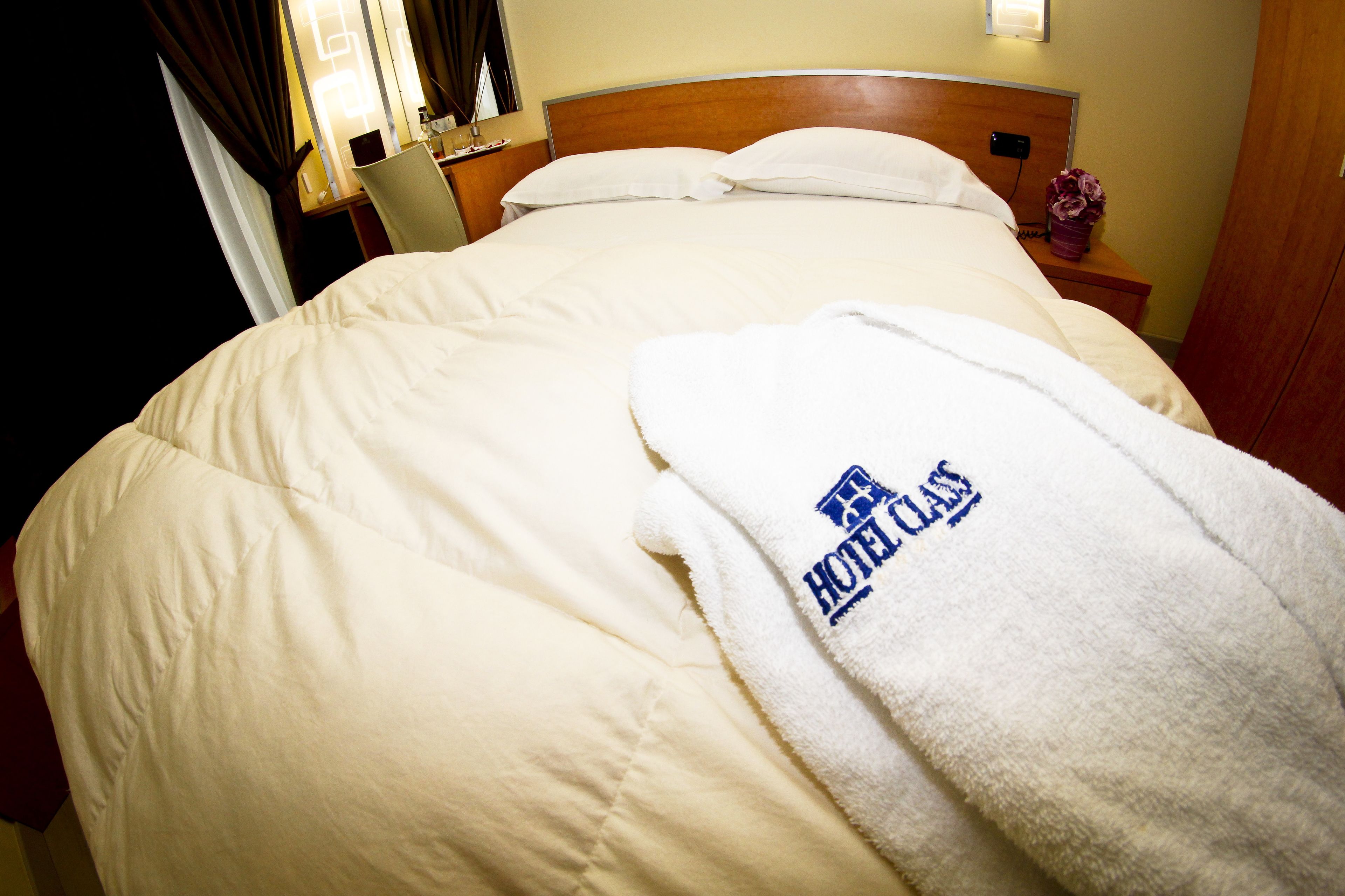 Un letto rifatto con un comofortino bianco e un asciugamano con il logo dell'hotel.