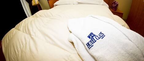A neatly made bed with a white comforter and a towel with a hotel logo.