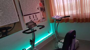 Una cyclette con display digitale, un poster appeso al muro e una finestra con tende leggere.