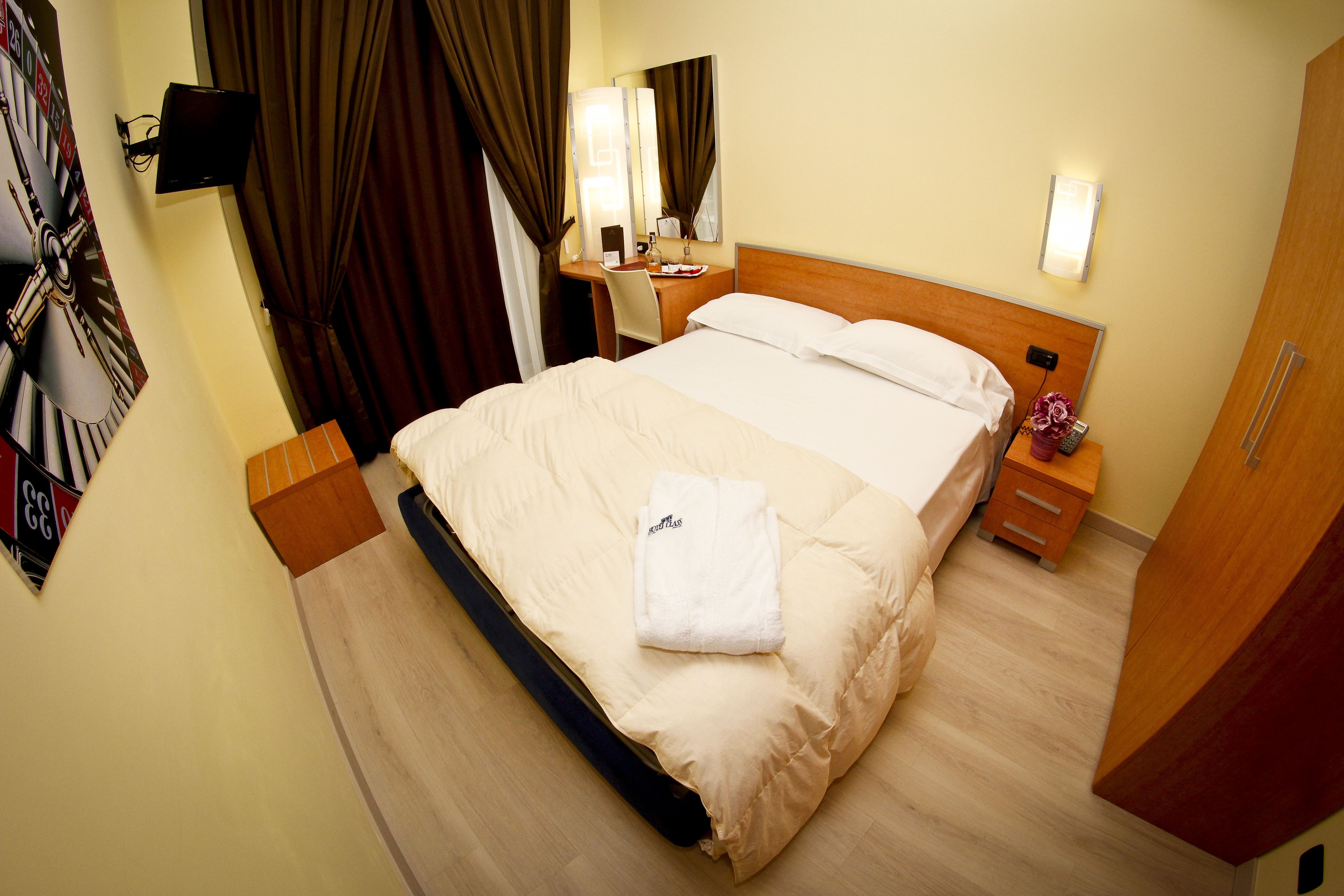 Une chambre d’hôtel équipée d’un lit, d’un bureau, d’une chaise, d’une table de chevet, d’un miroir et d’un téléviseur fixé au mur.