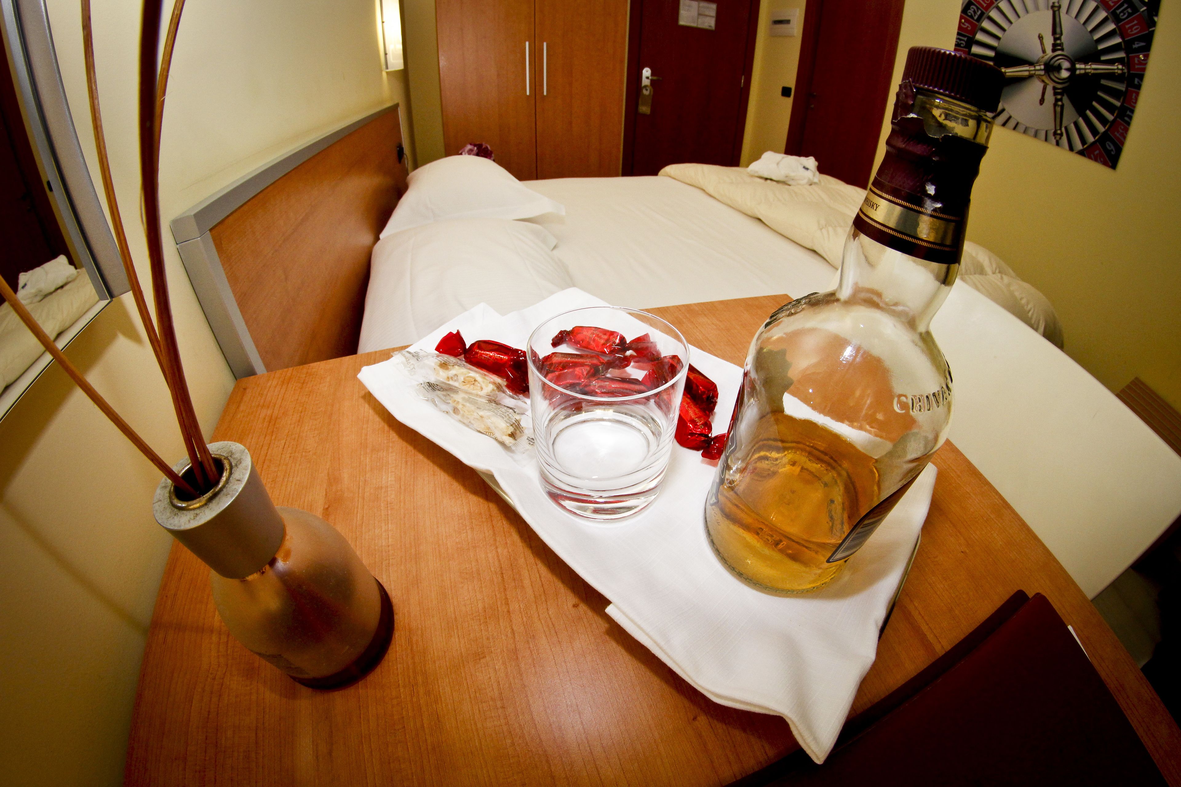 A hotel room with a wooden bed, a bedside table with a bottle, glasses, and strawberries.