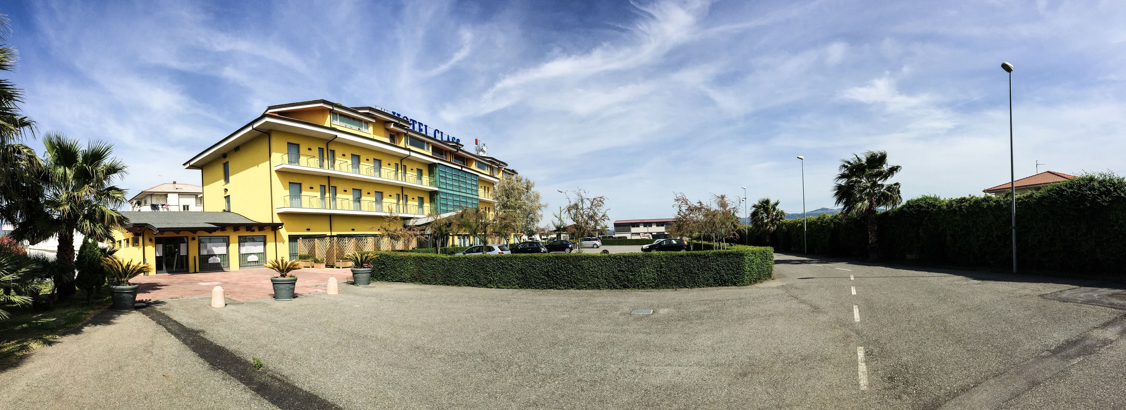 A hotel with a yellow facade, multiple floors, and a parking area with cars.