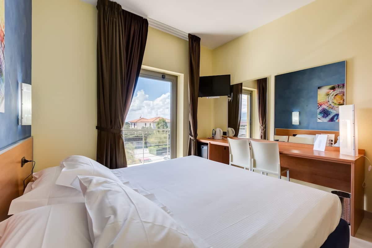 A hotel room with a large bed, a desk, a chair, a flat-screen TV, and a window with curtains.
