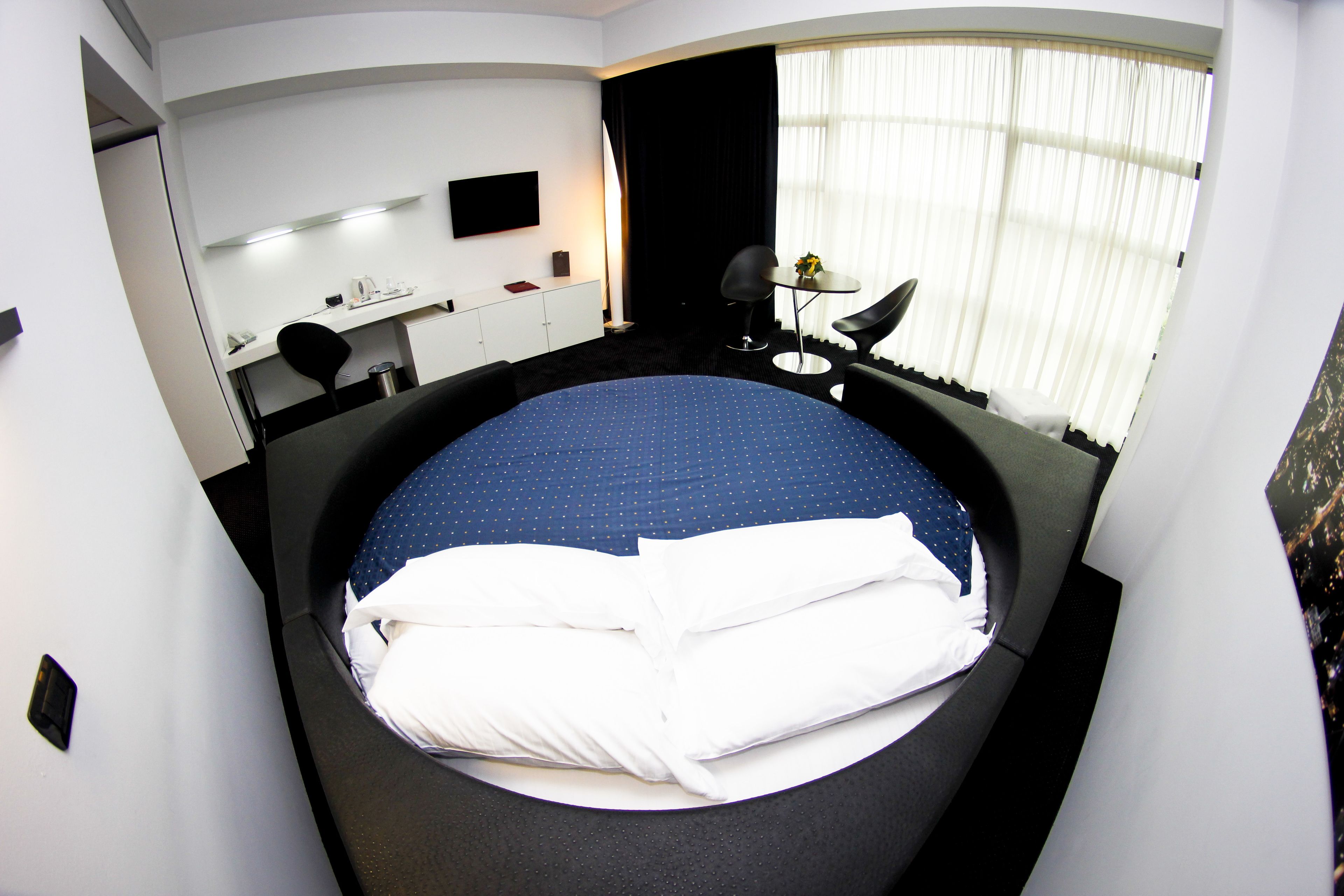 A modern hotel room with a large bed, a desk, a chair, a TV, and a window with curtains.
