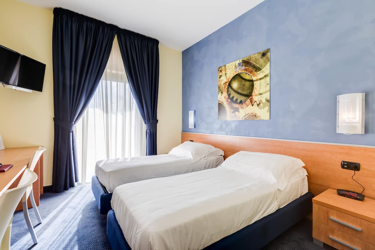 A hotel room with two beds, a desk, a chair, a TV, and a painting on the wall.