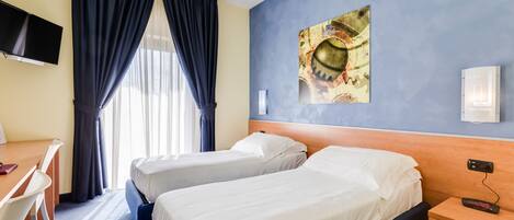 A hotel room with two beds, a desk, a chair, a TV, and a painting on the wall.