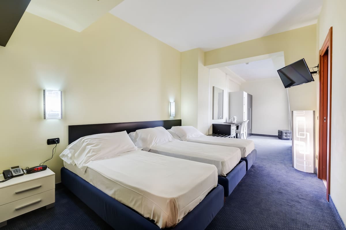 A hotel room with two beds, a desk, a chair, a TV mounted on the wall, and a window.