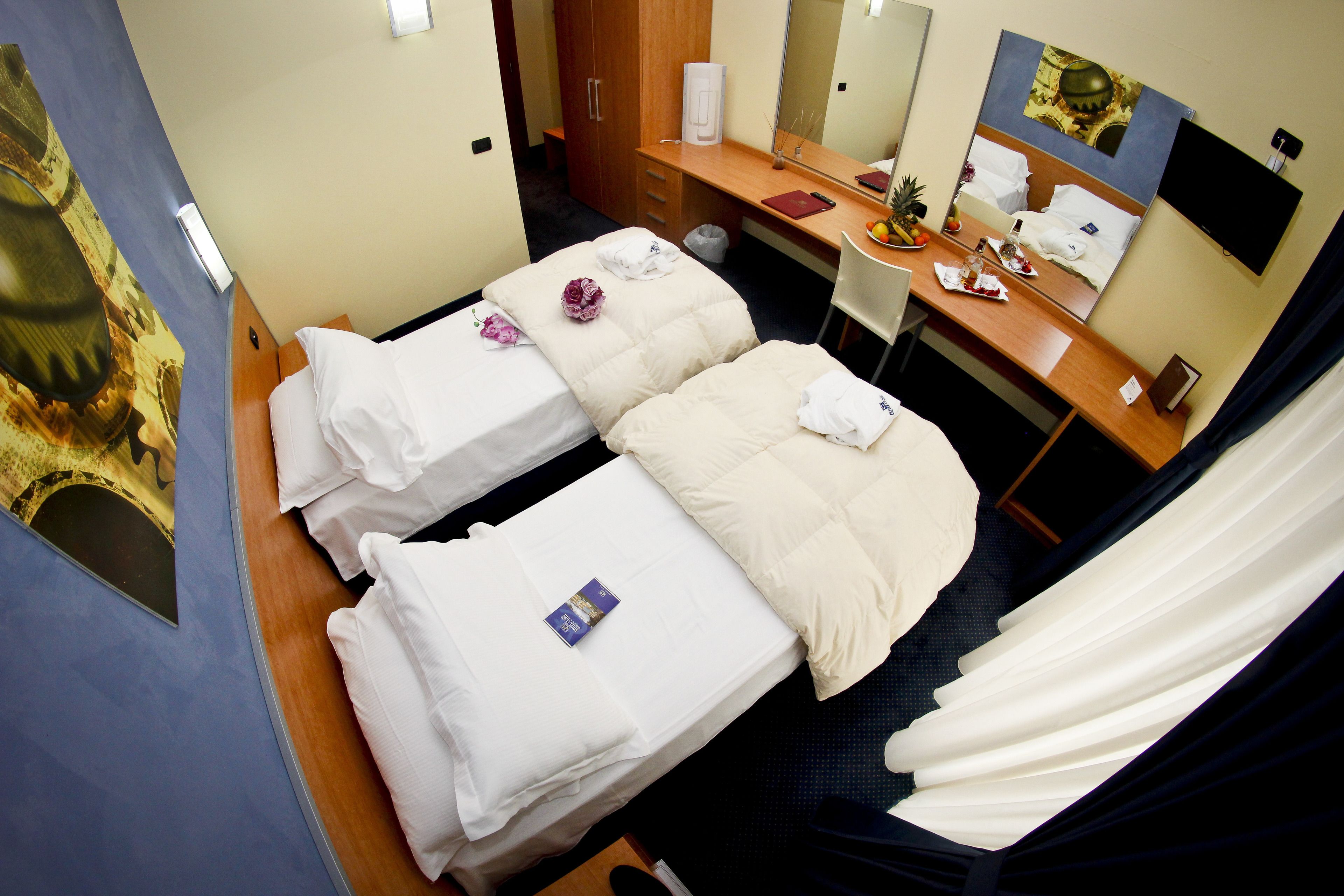 Ein Hotelzimmer mit zwei Betten, einem Schreibtisch mit Spiegel, einem Fernseher und einem Badezimmer.