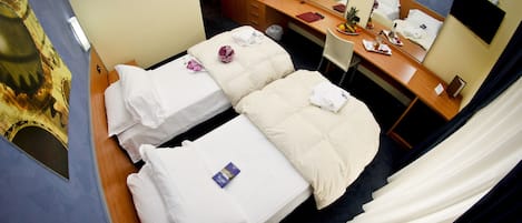 Ein Hotelzimmer mit zwei Betten, einem Schreibtisch mit Spiegel, einem Fernseher und einem Badezimmer.