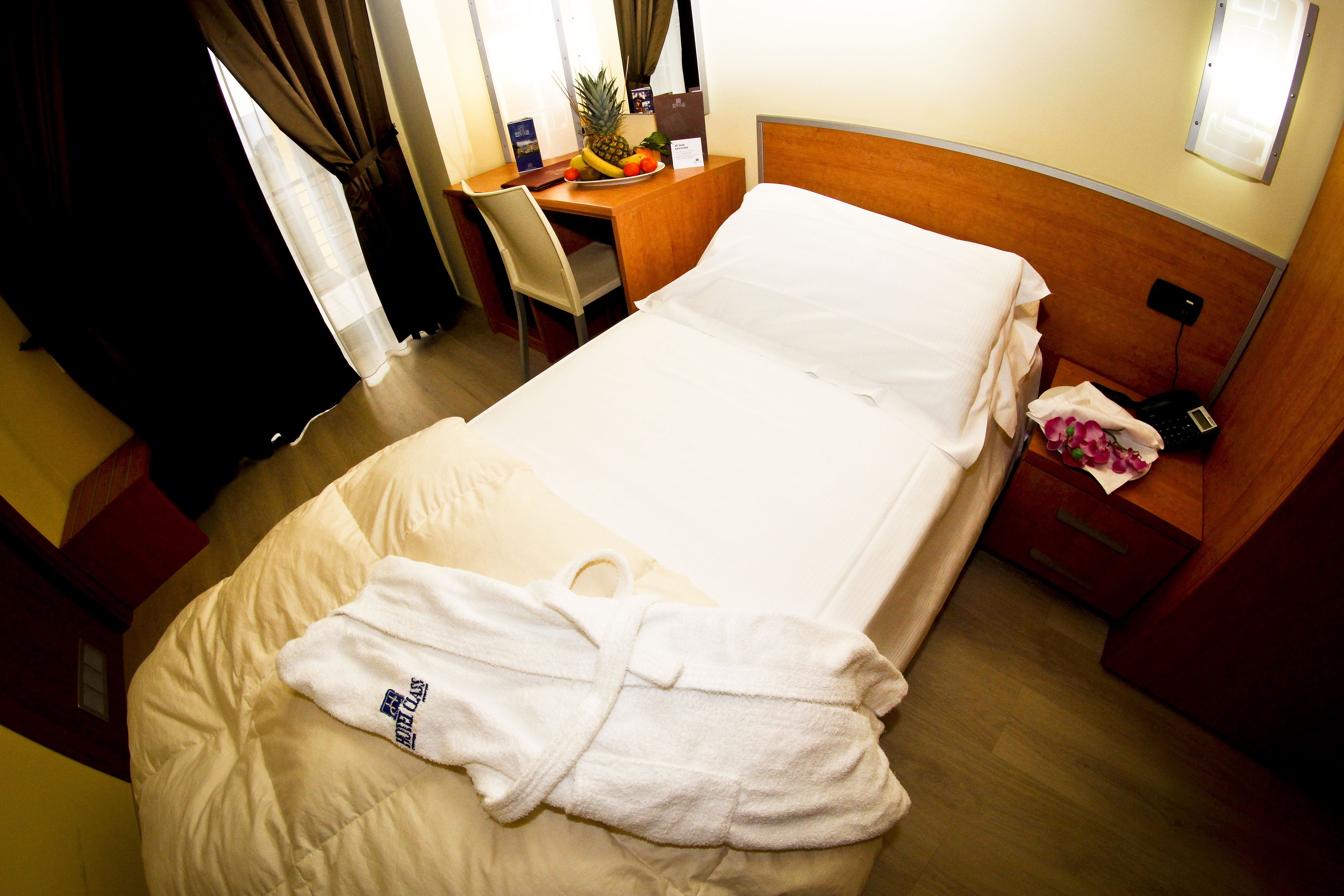Une chambre d’hôtel comprenant un lit, un bureau avec une chaise, une petite table avec des fruits et une table de chevet avec un téléphone.