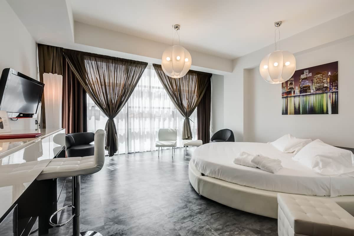 A modern hotel room with a large bed, a desk, a chair, and a TV.