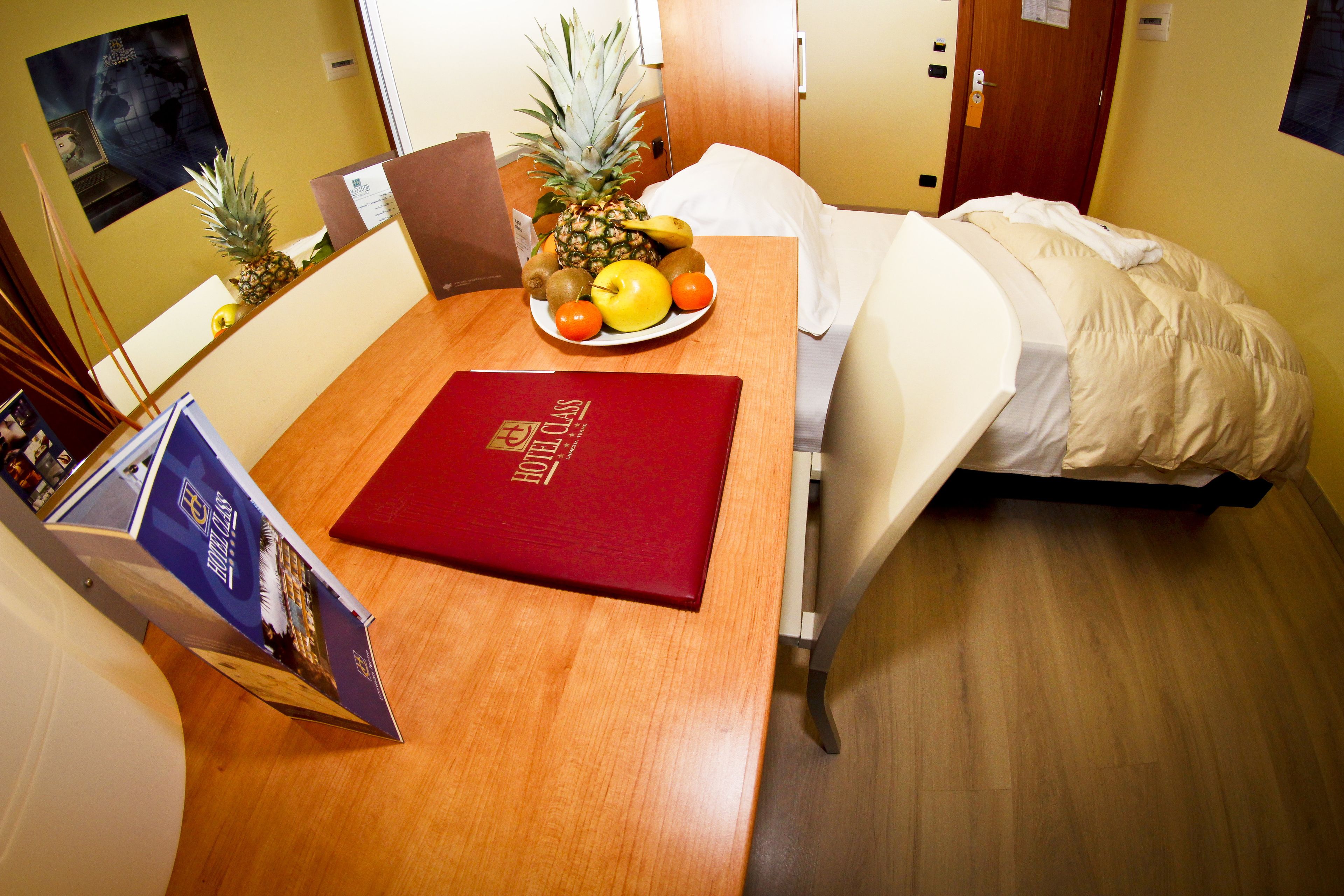 A hotel room with a bed, a small table with a fruit bowl, a red booklet, and a brochure on the table.