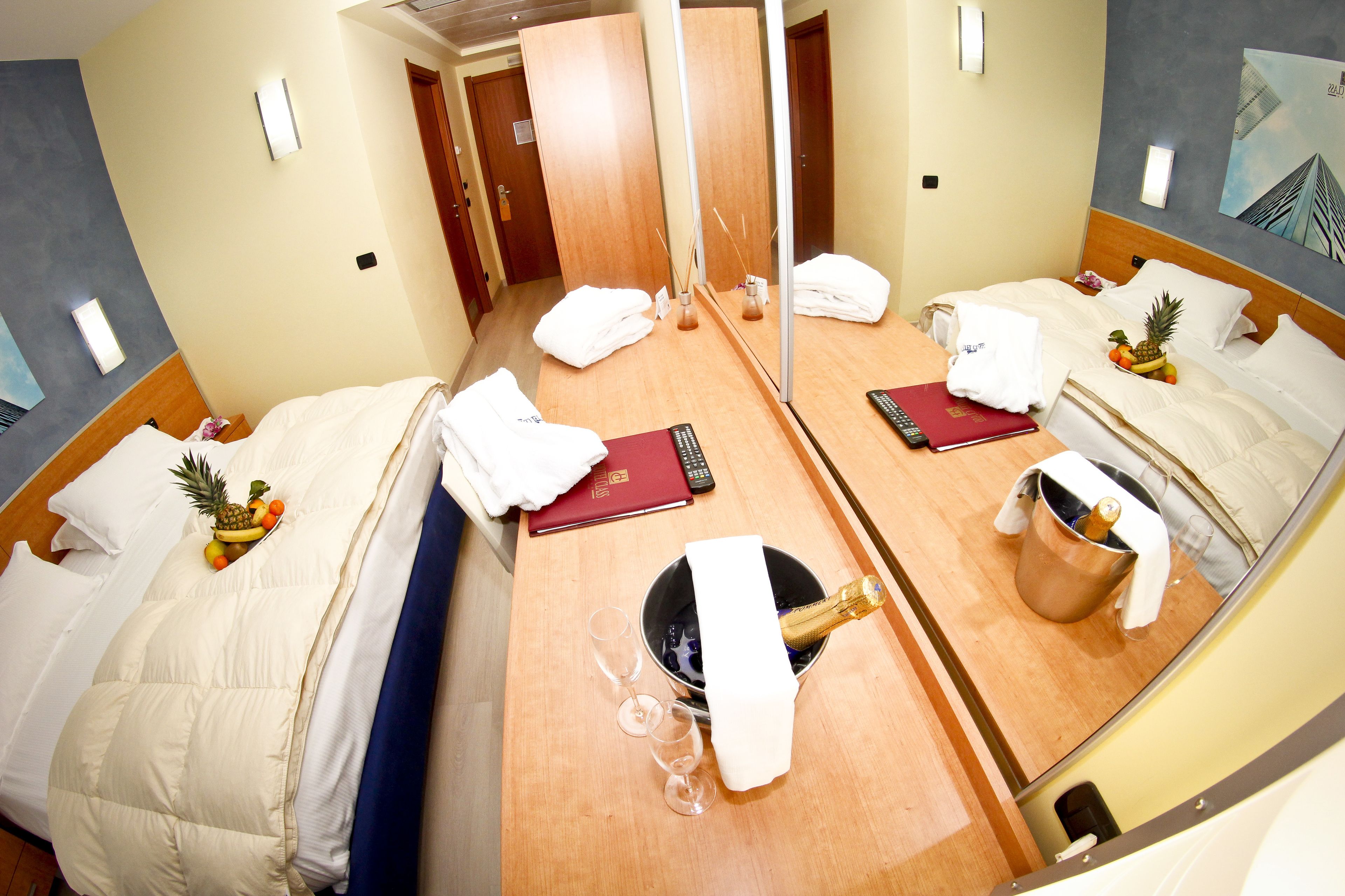 Une chambre d’hôtel avec deux lits, un minibar, un miroir et une porte donnant sur une autre chambre.
