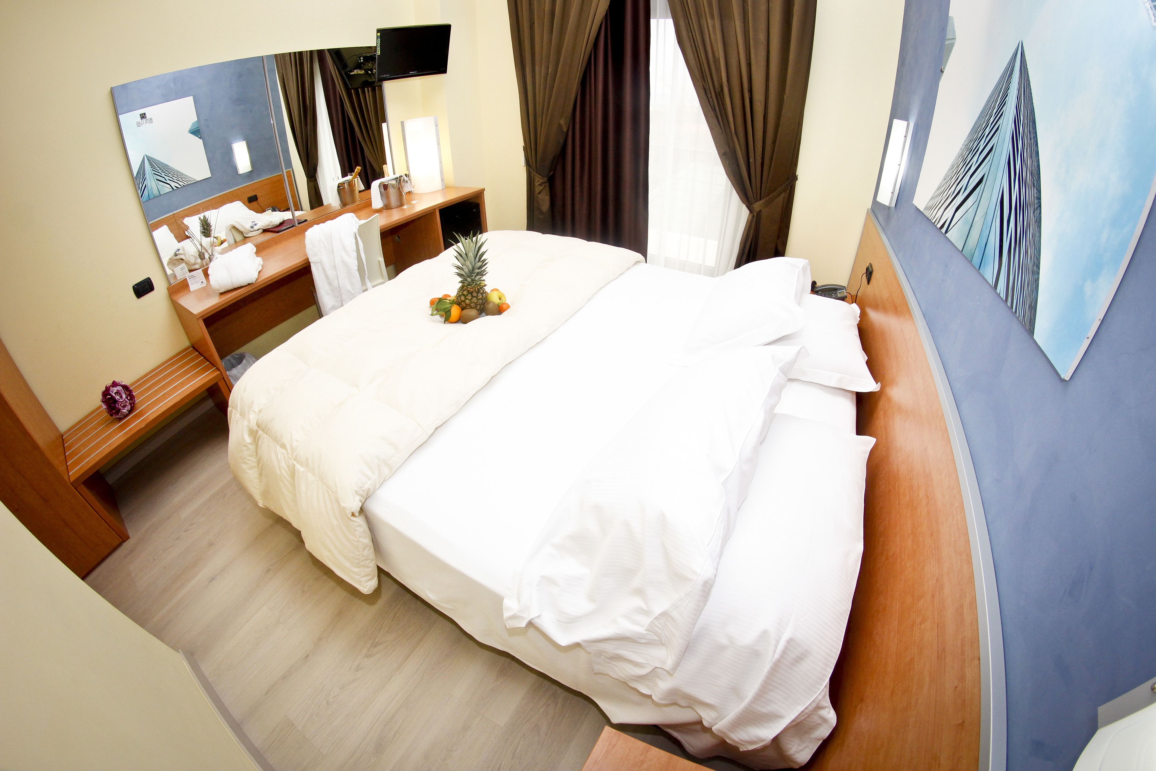 Ein Hotelzimmer mit einem Bett, einem Schreibtisch mit Telefon und einer Vase, einem Spiegel und einem Bild an der Wand.