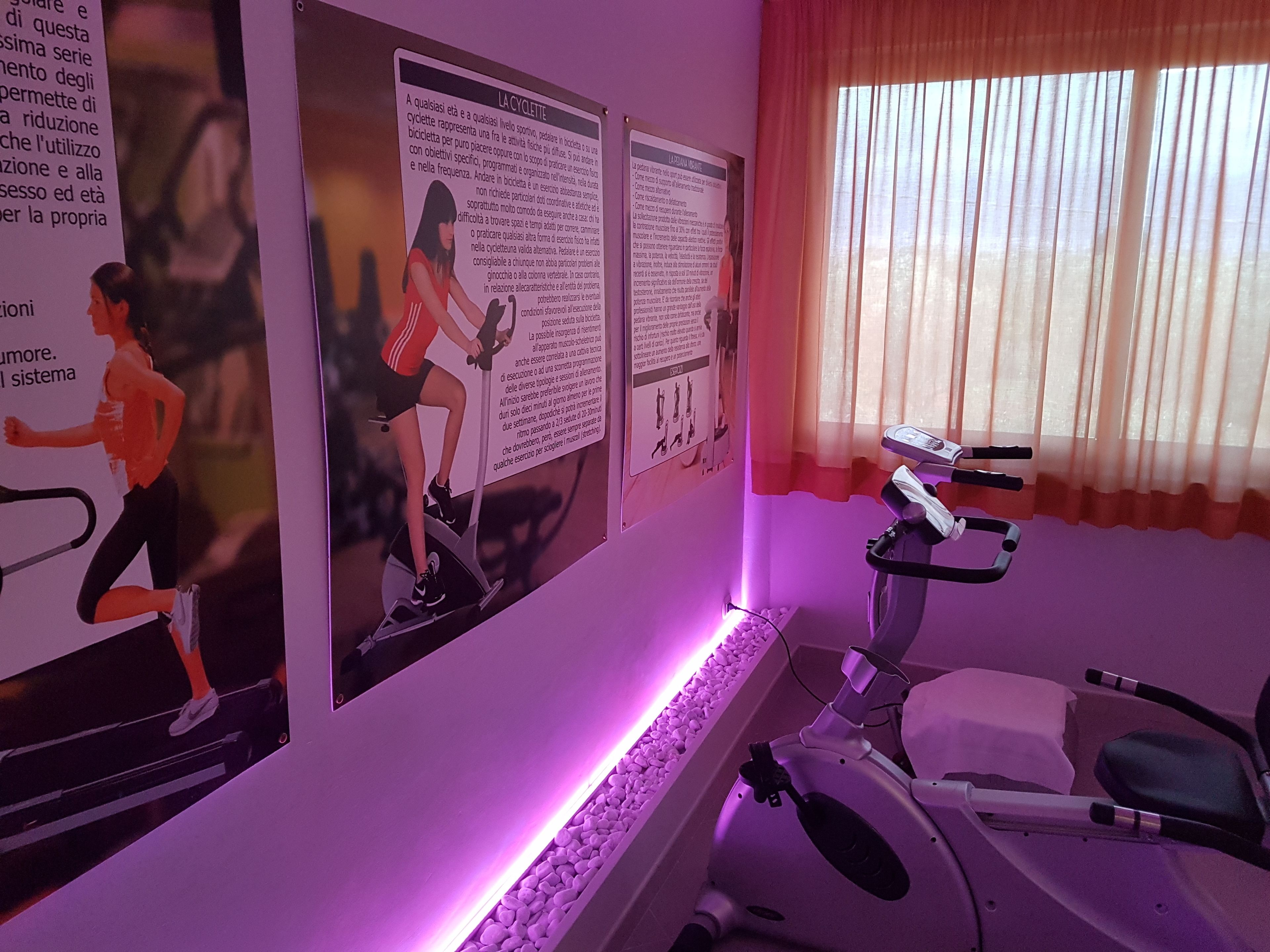 Een kamer met een hometrainer, posters aan de muur en een raam met gordijnen.