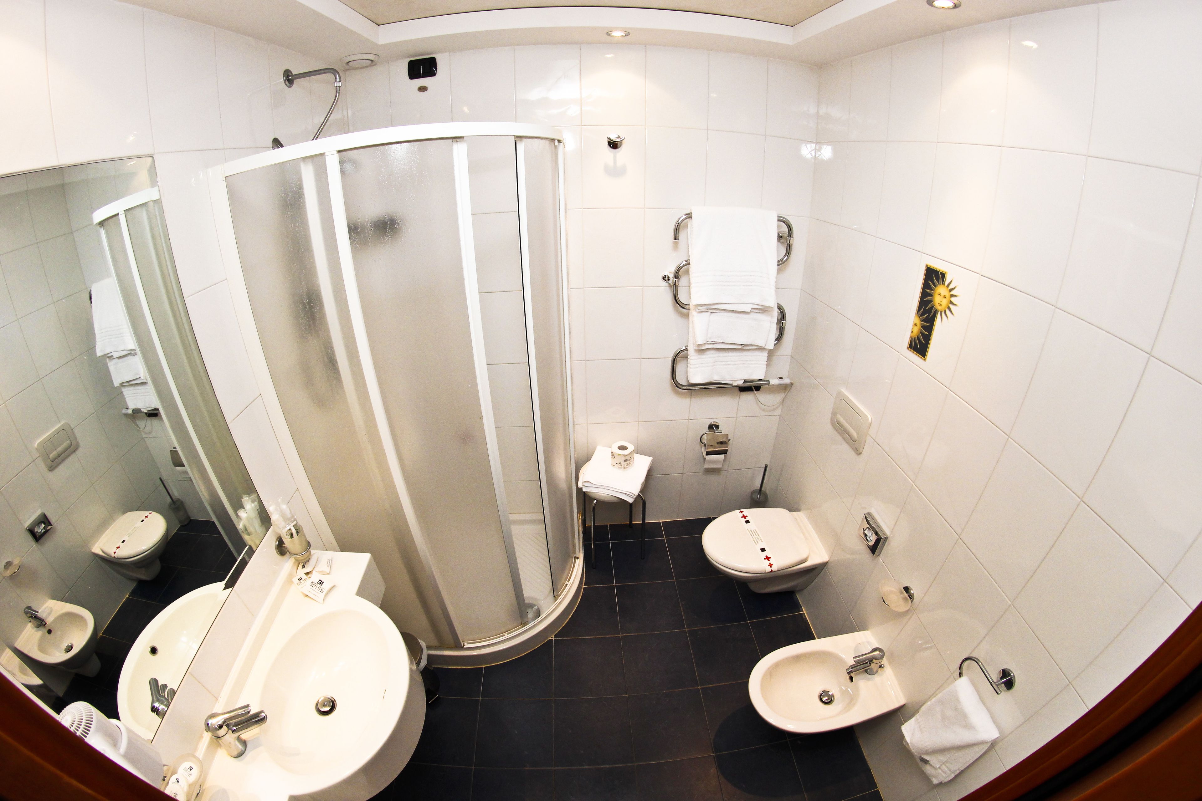 A modern bathroom with a glass-enclosed shower, two sinks, a toilet, and a bidet.