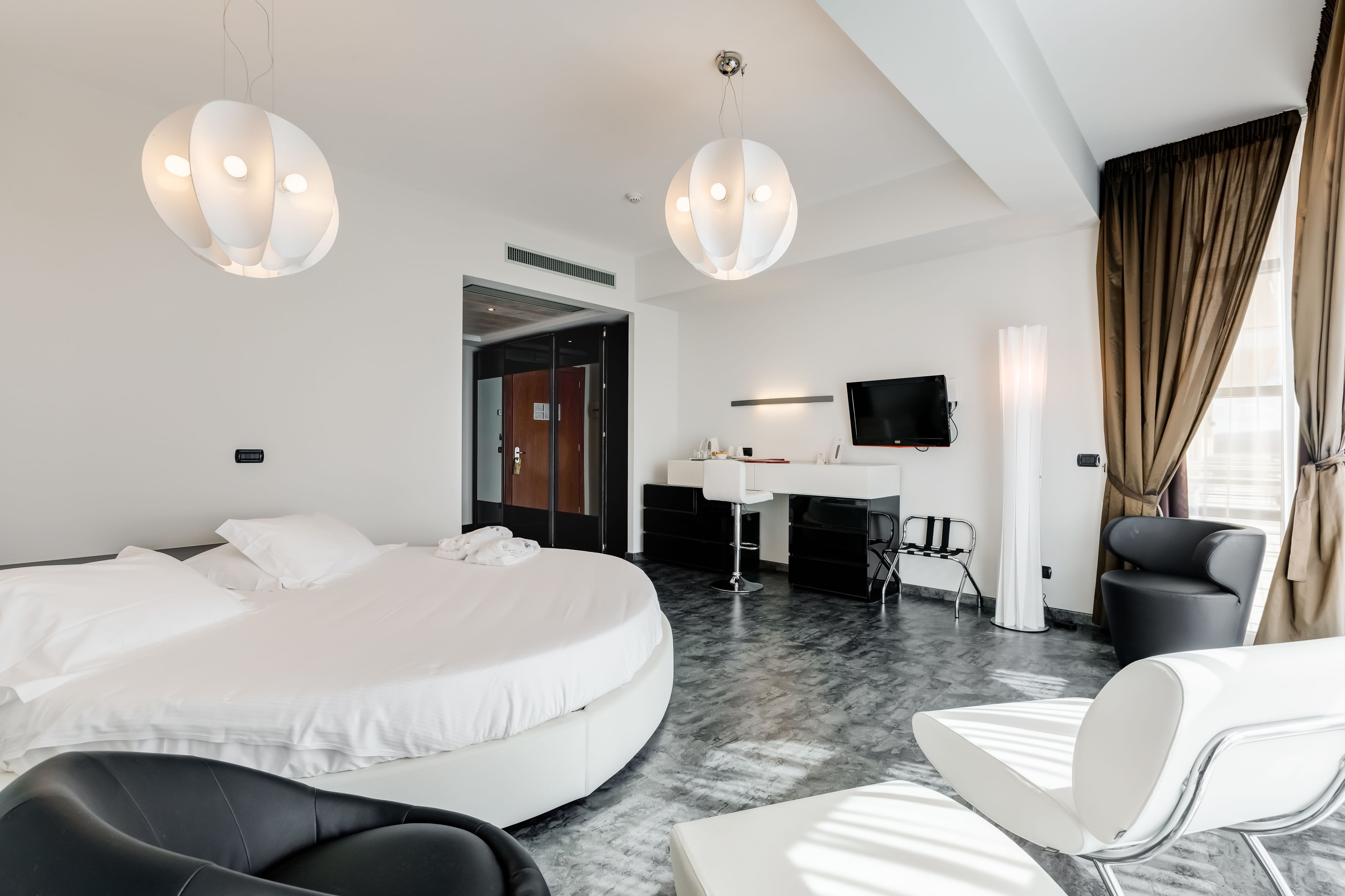 A modern hotel room with a large bed, a desk with a chair, a TV, and a seating area with chairs.
