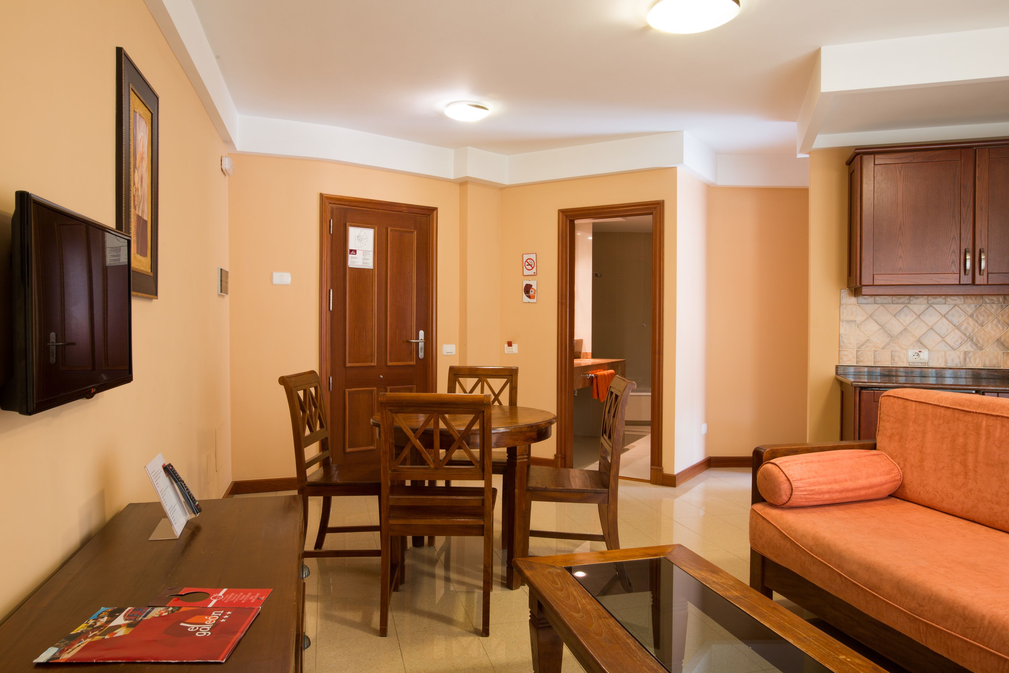 Un comedor con una mesa y sillas de madera, un sofá y un televisor montado en la pared.