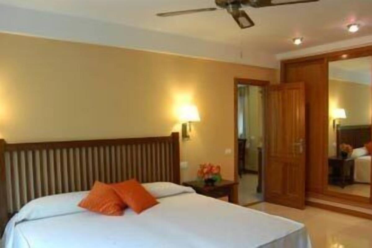 A hotel room with a bed, a ceiling fan, a nightstand, and a mirror.