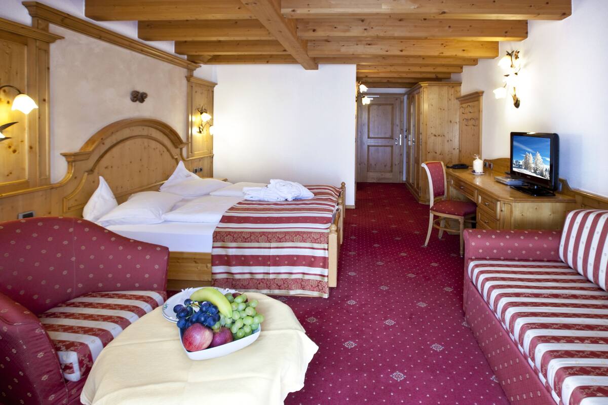 A hotel room with two beds, a desk with a television, a chair, and a fruit bowl on the table.