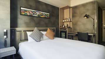A hotel room with a large bed, a desk, a chair, a lamp, a painting on the wall, and a telephone.