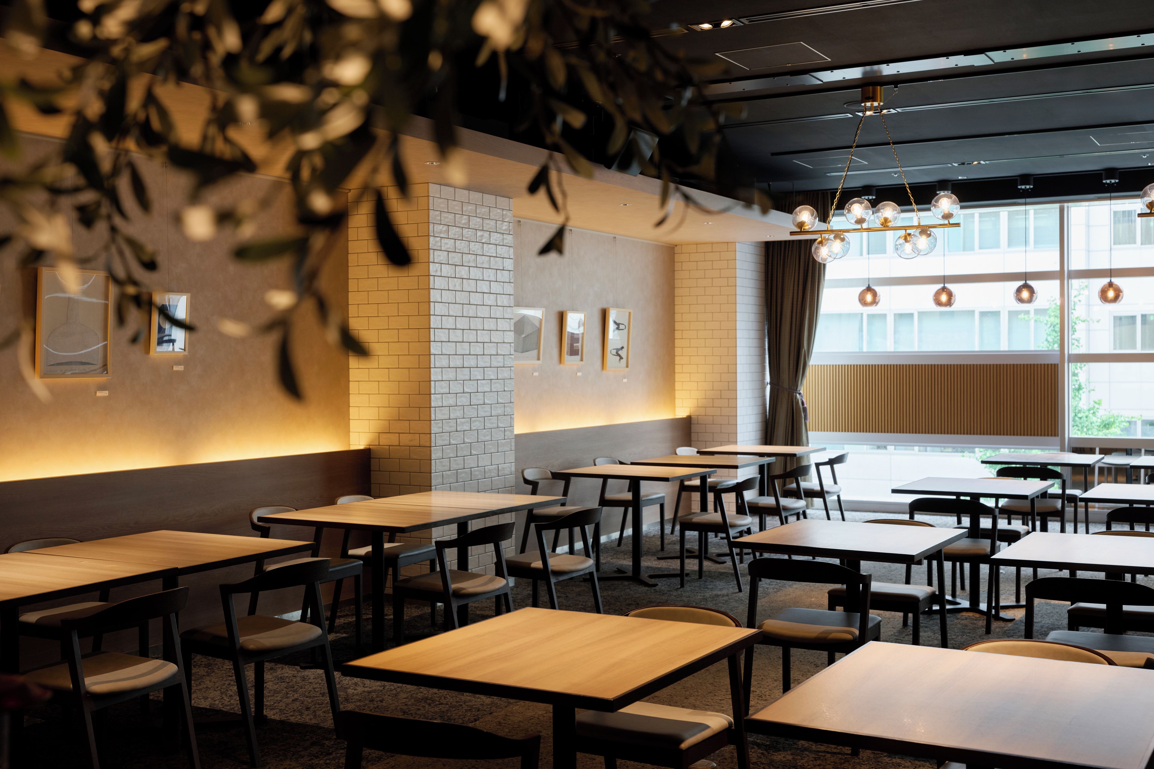 A modern restaurant interior with wooden tables and chairs, brick walls, and pendant lighting.