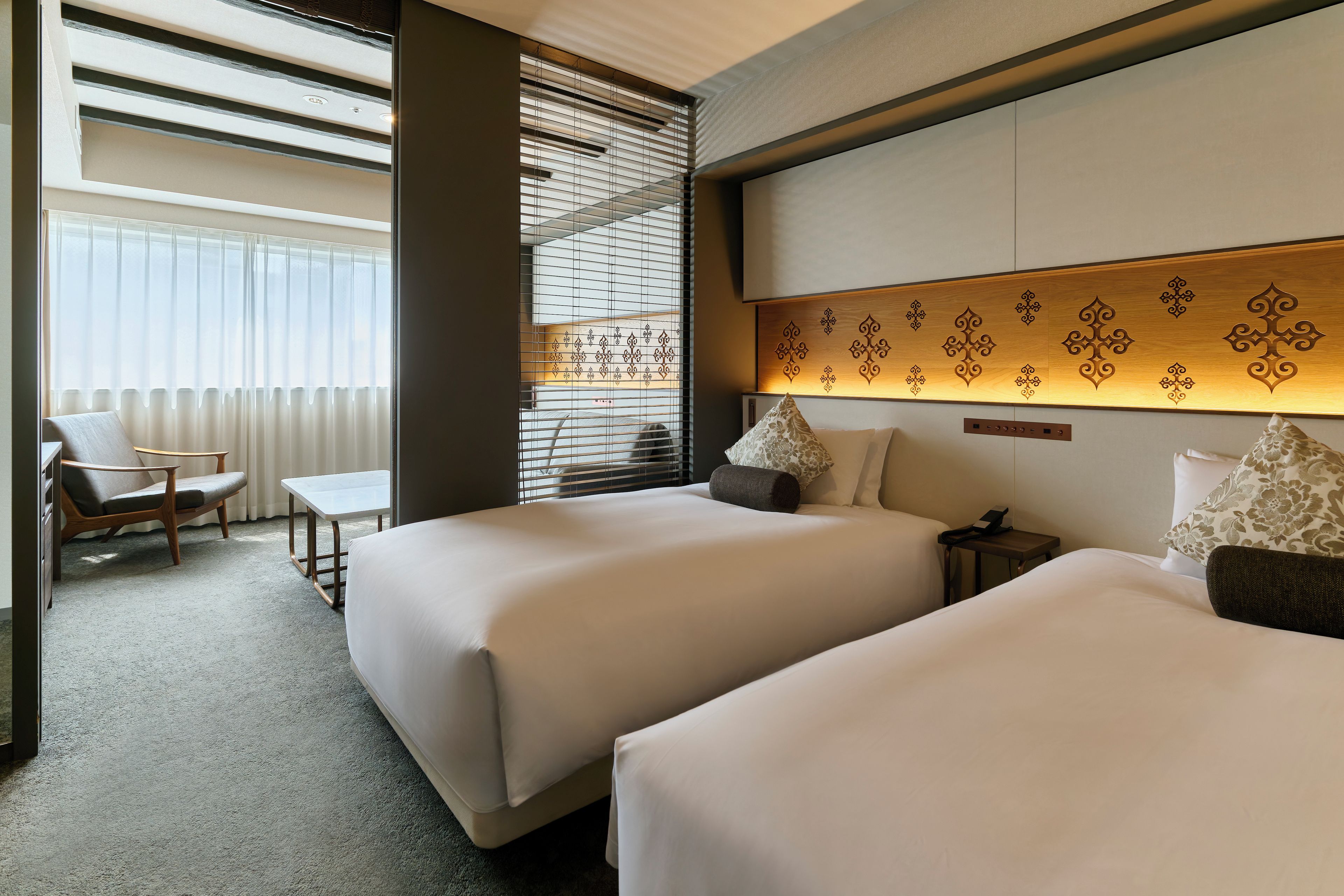 A hotel room with two beds, a desk, a chair, and a window with blinds.