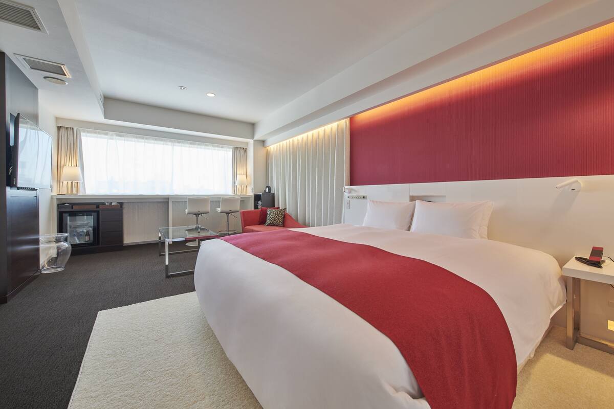 A hotel room with a large bed, a flat-screen TV, a minibar, and a seating area with a glass table.