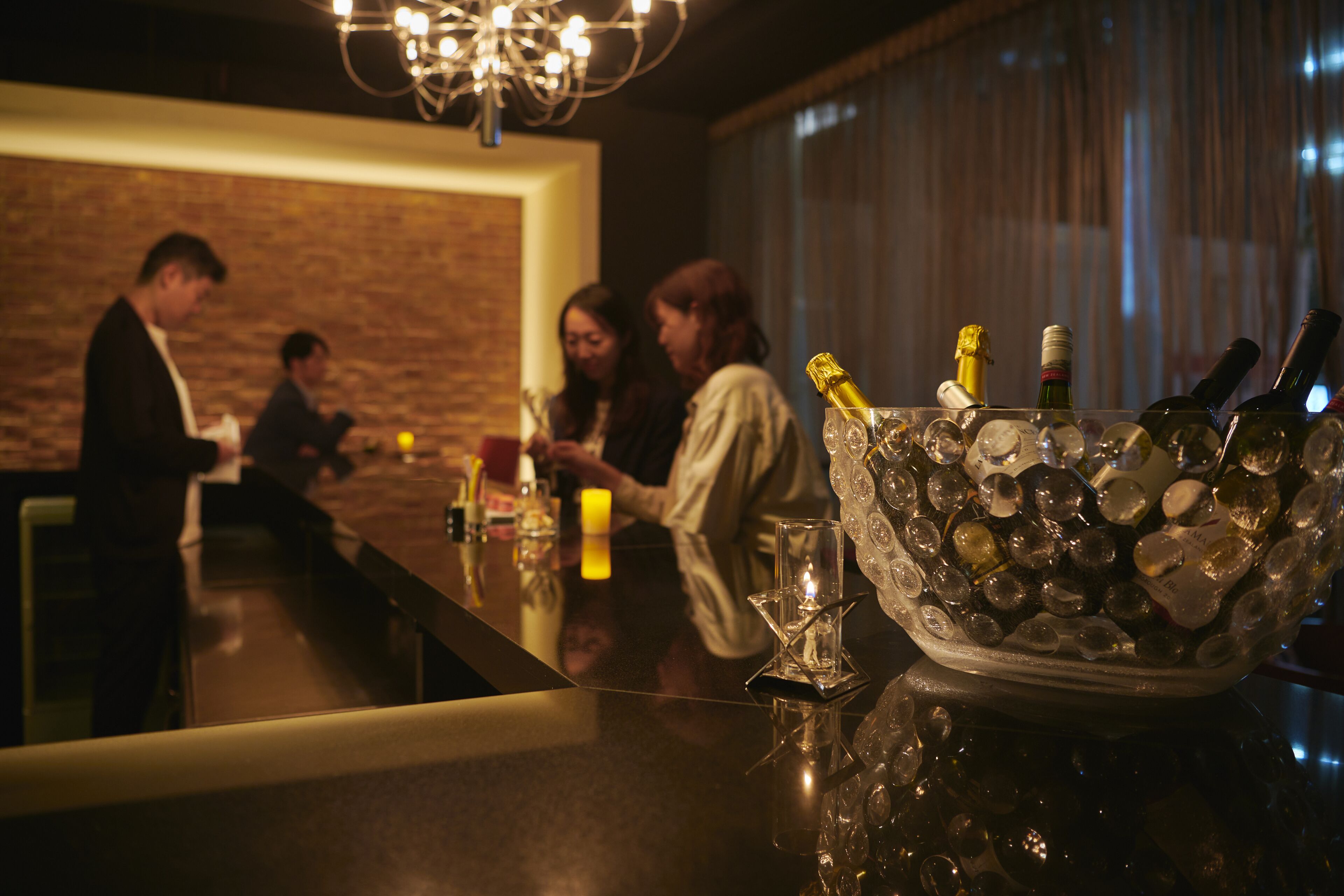 A bar area with a reflective countertop, a glass bowl filled with ice and bottles, and a brick wall in the background.