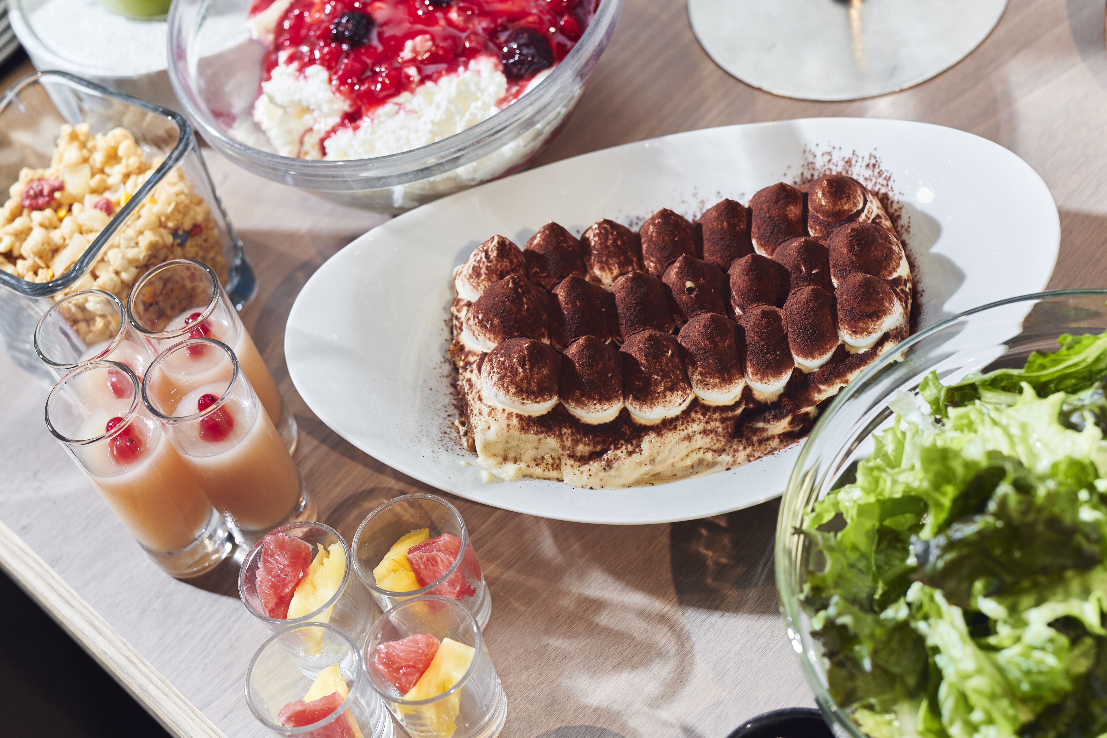 A dessert tray with tiramisu, fruit juices, and a salad.