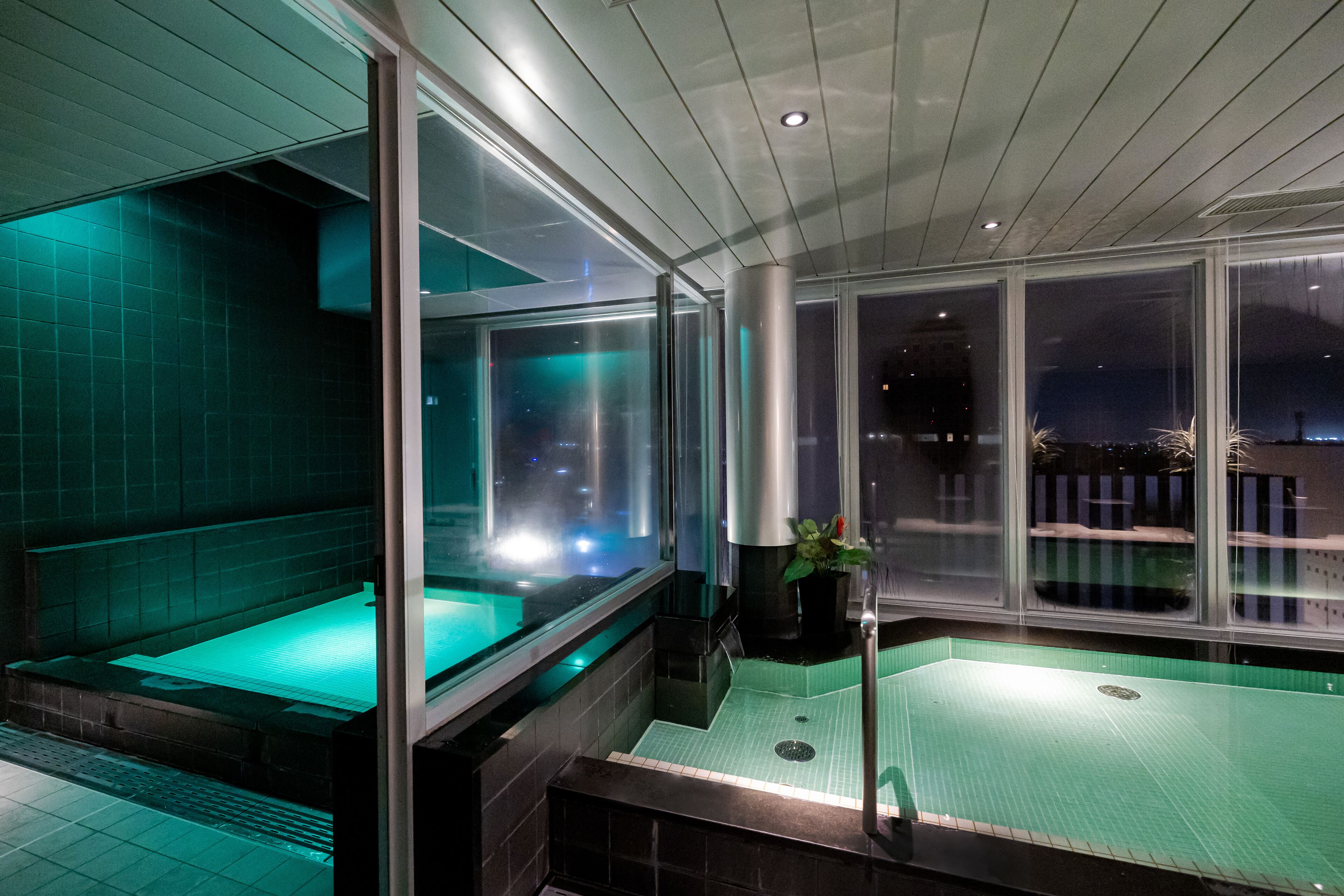 A modern spa area with a hot tub, a separate relaxation area, and a view of the city at night.