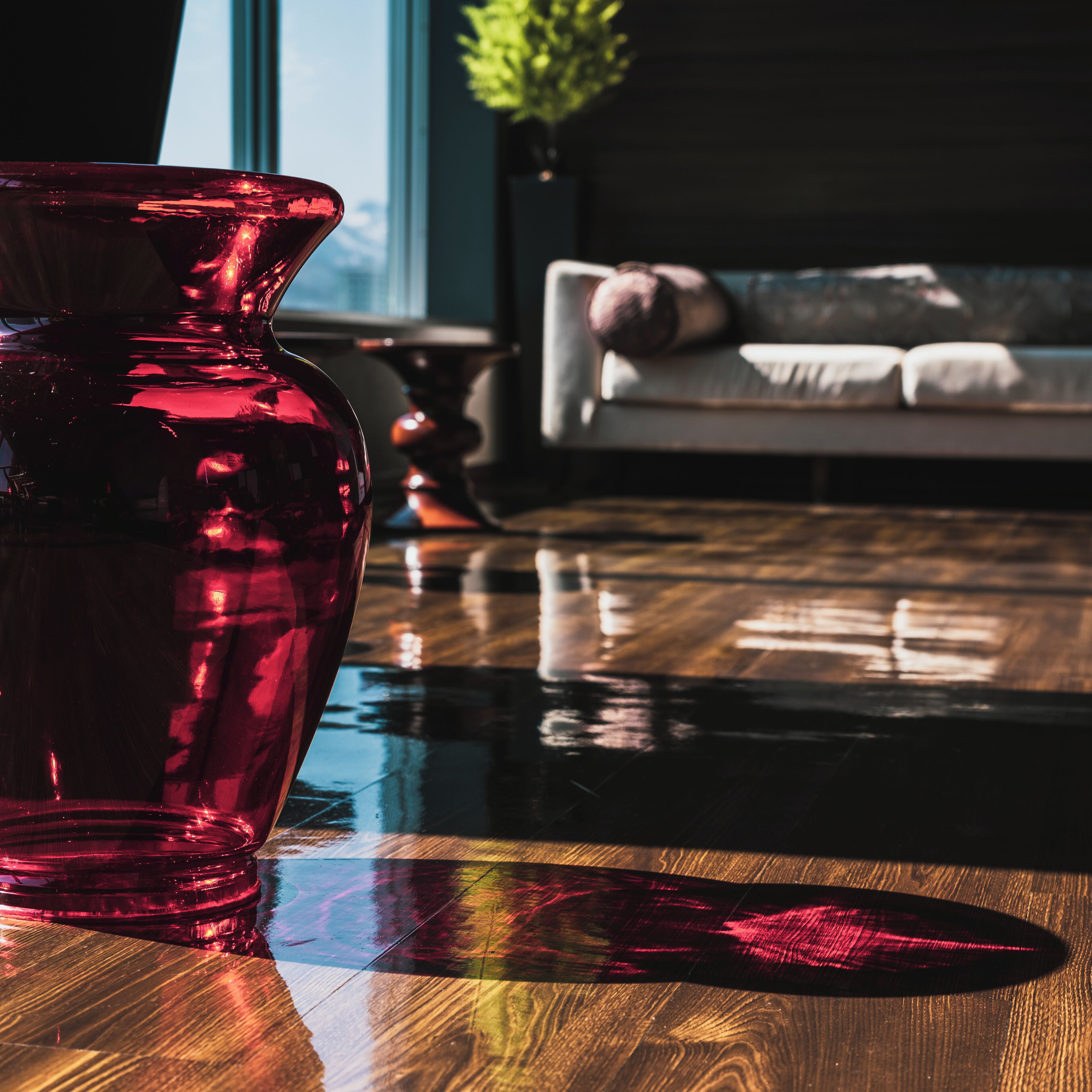 A red vase on a reflective wooden table in a room with a sofa and a plant in the background.