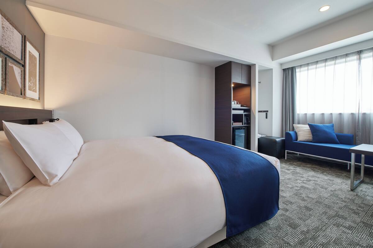 A hotel room with a large bed, a sofa, a small table, and a desk.