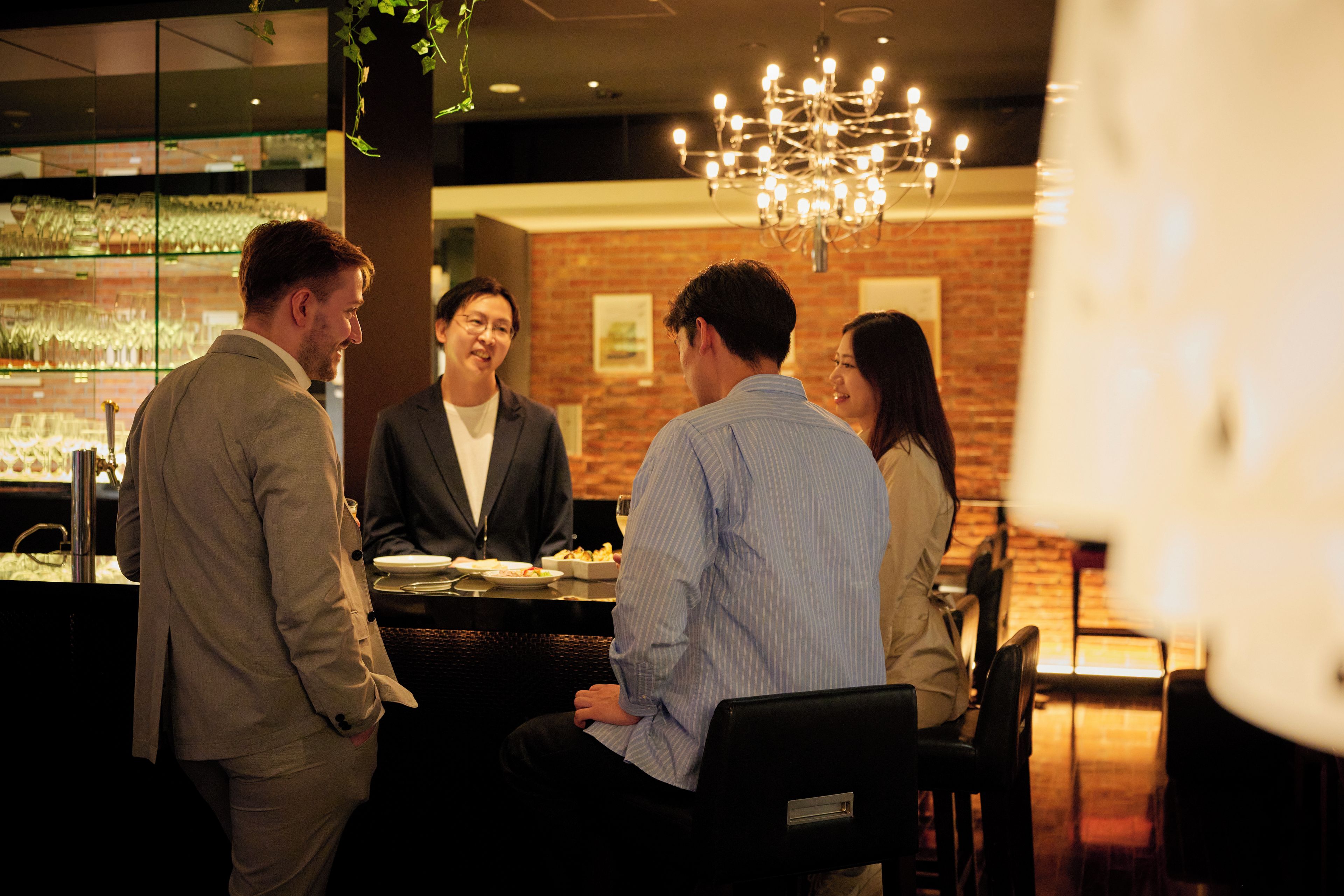 A group of people seated at a table in a restaurant with a brick wall and a chandelier in the background.