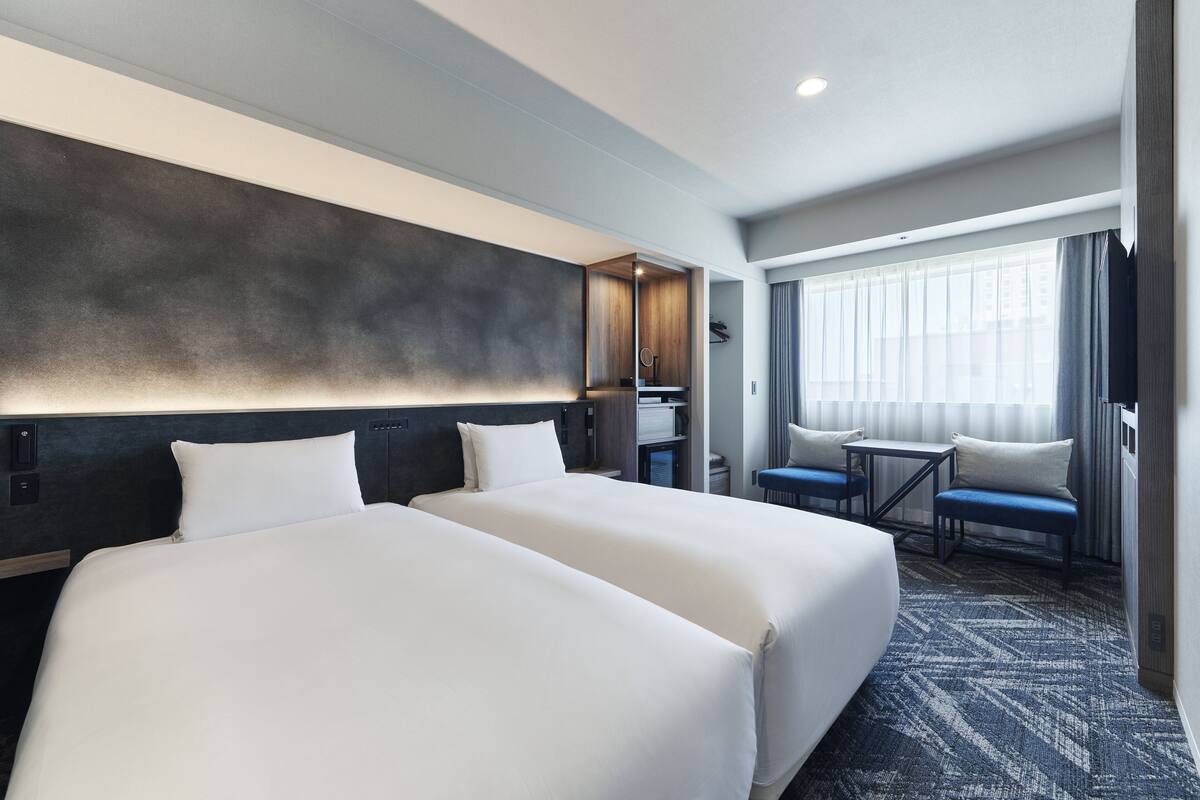 A hotel room with two beds, a desk, and a small seating area.