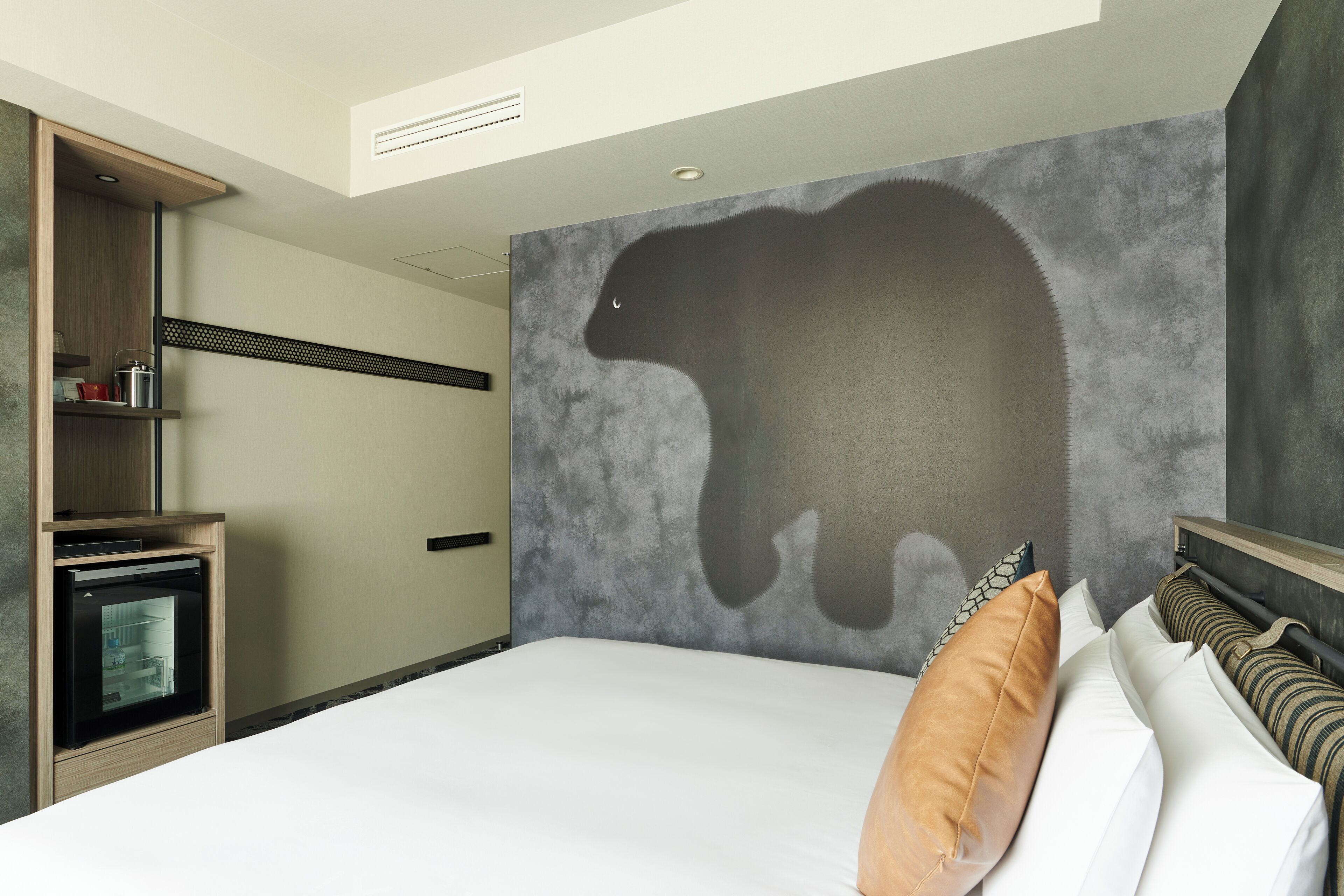 Habitación de hotel con cama, televisión empotrada, armario y un mural grande con un oso.