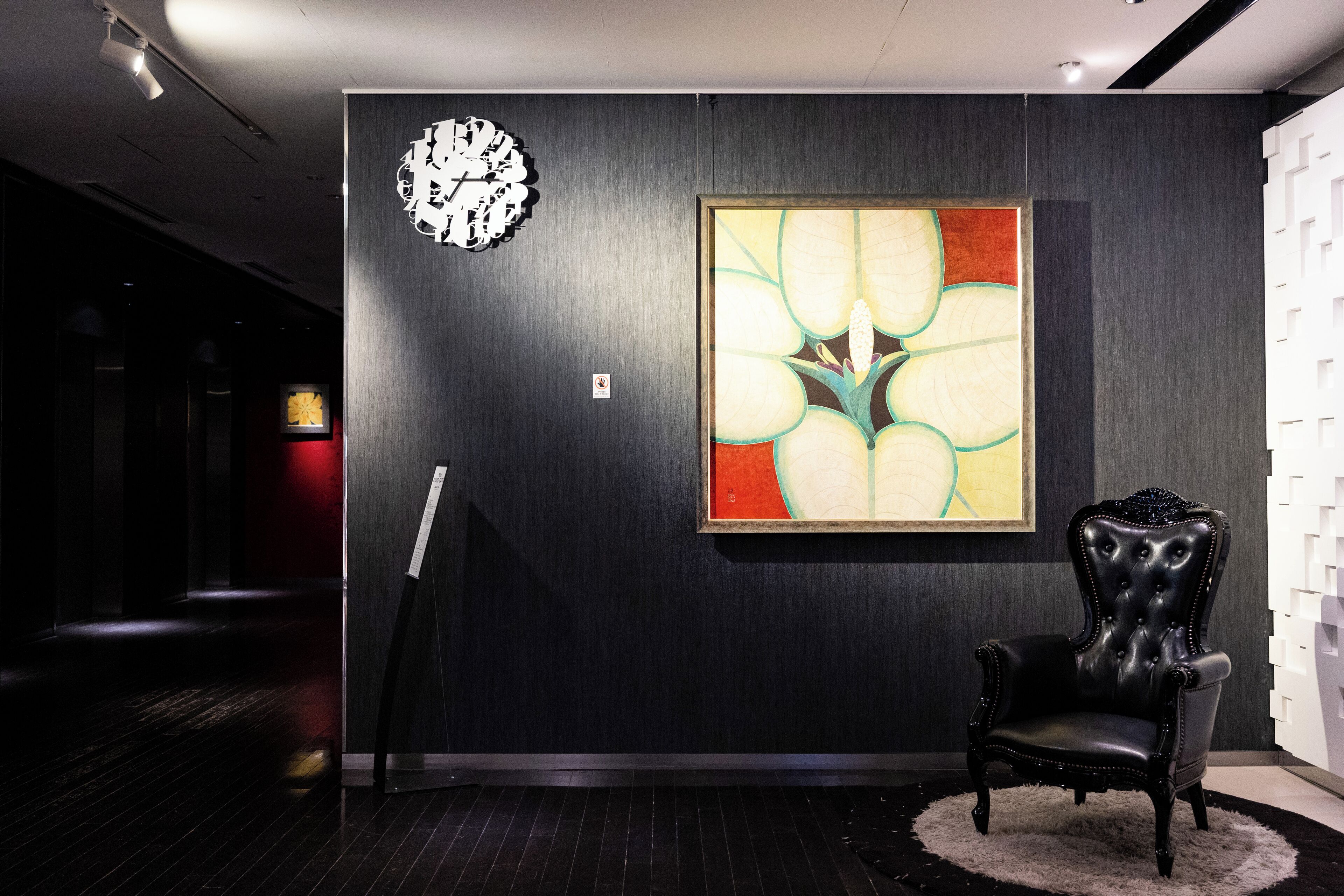 A modern interior with a dark wood panel wall, a large abstract painting, a classic black leather armchair, and a clock.