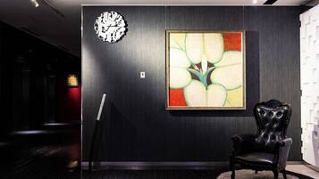 A modern interior with a dark wood panel wall, a large abstract painting, a classic black leather armchair, and a clock.