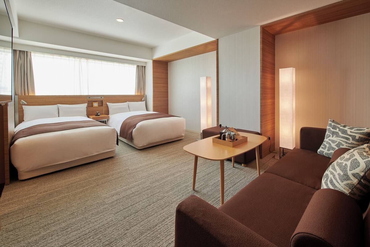 A hotel room with two beds, a sofa, a small table, and a lamp.